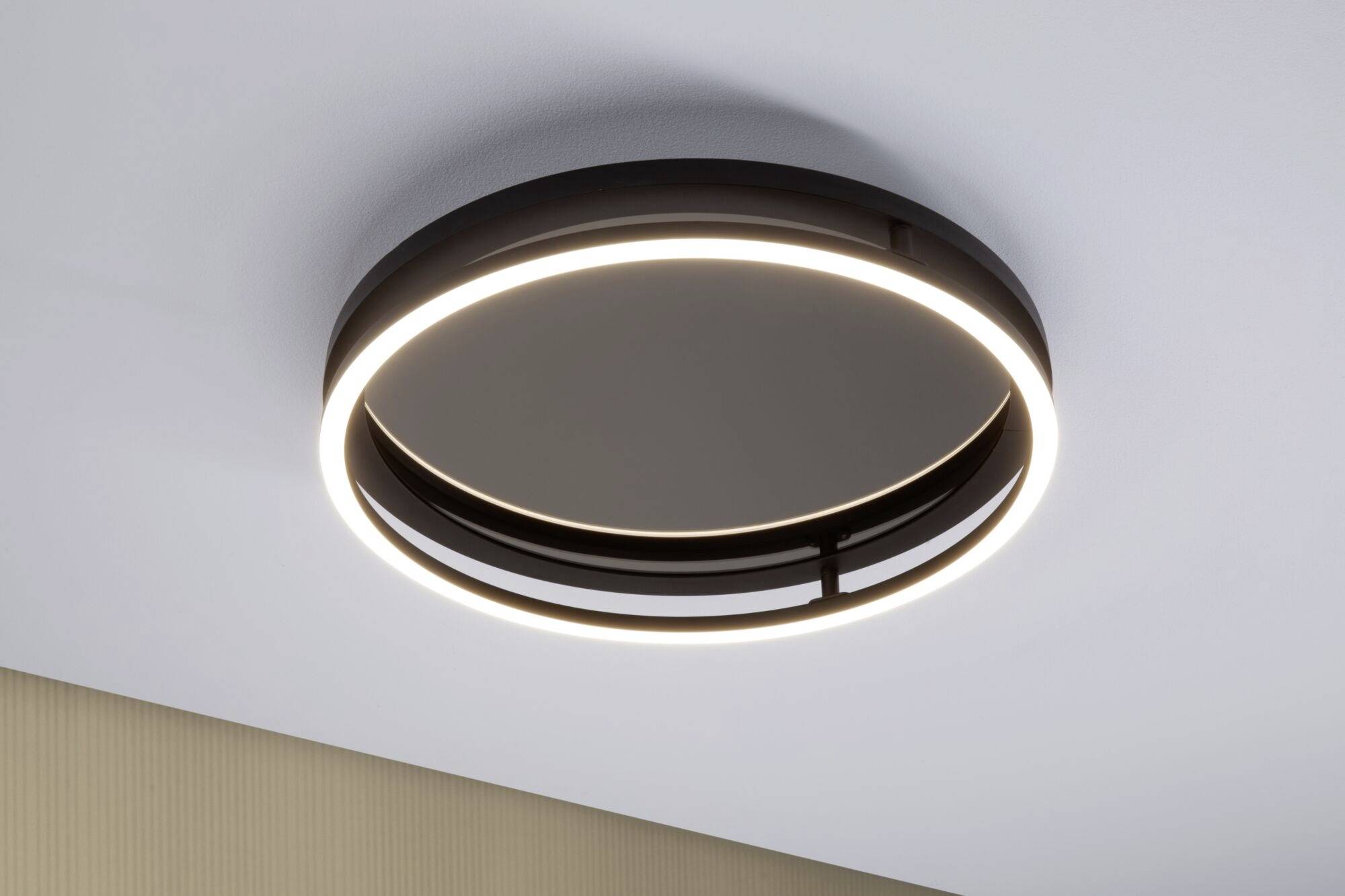 Okrągła lampa sufitowa o nowoczesnym designie, z czarną ramą i świecącym pierścieniem LED zamontowana na suficie.