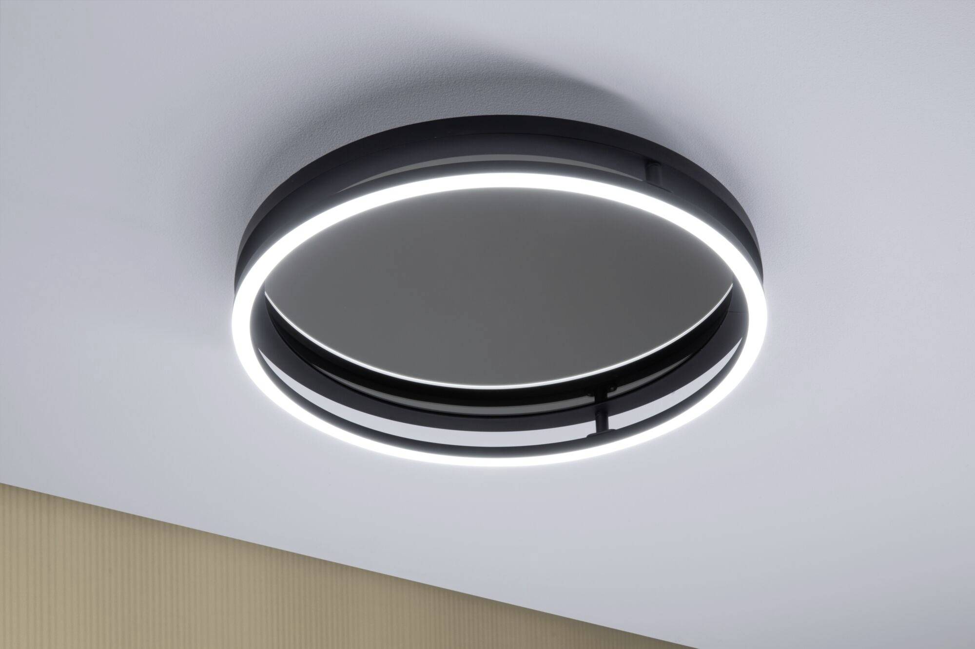 Okrągła, nowoczesna lampa sufitowa z pierścieniem LED, zamontowana w minimalistycznym wnętrzu.