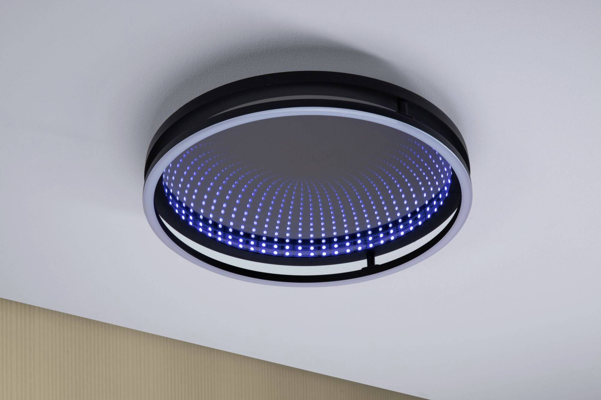 Okrągła, nowoczesna lampa sufitowa z niebieskim pierścieniem LED zamontowana na białym suficie, zapewnia klimatyczne oświetlenie.