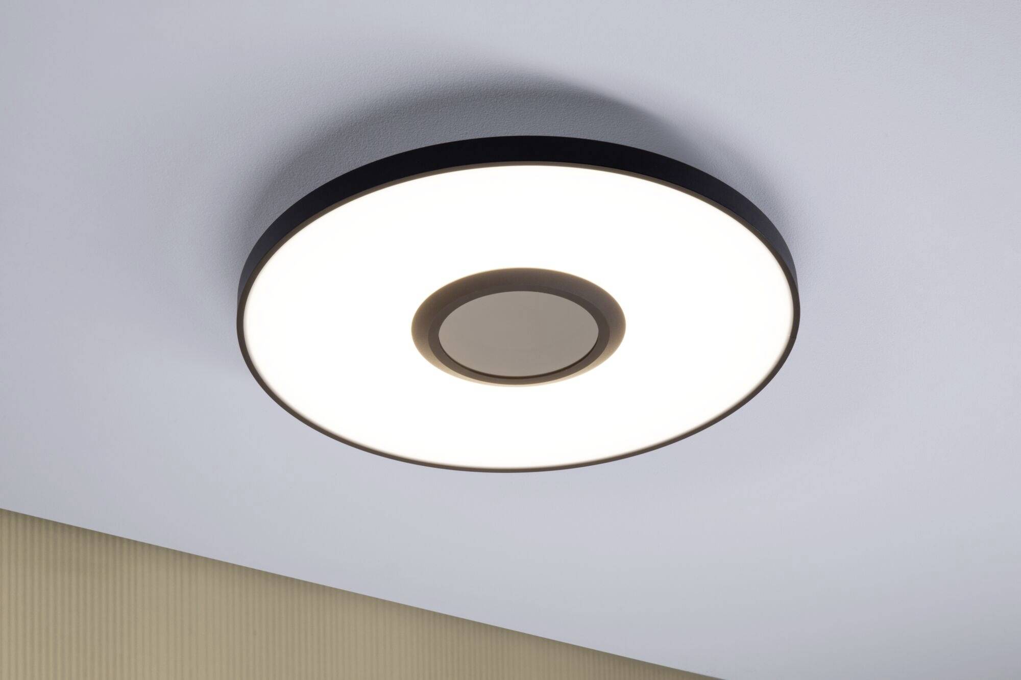 Okrągła lampa sufitowa z czarną ramką i centralnym kołem, oświetlająca pomieszczenie, o nowoczesnym i minimalistycznym designie.