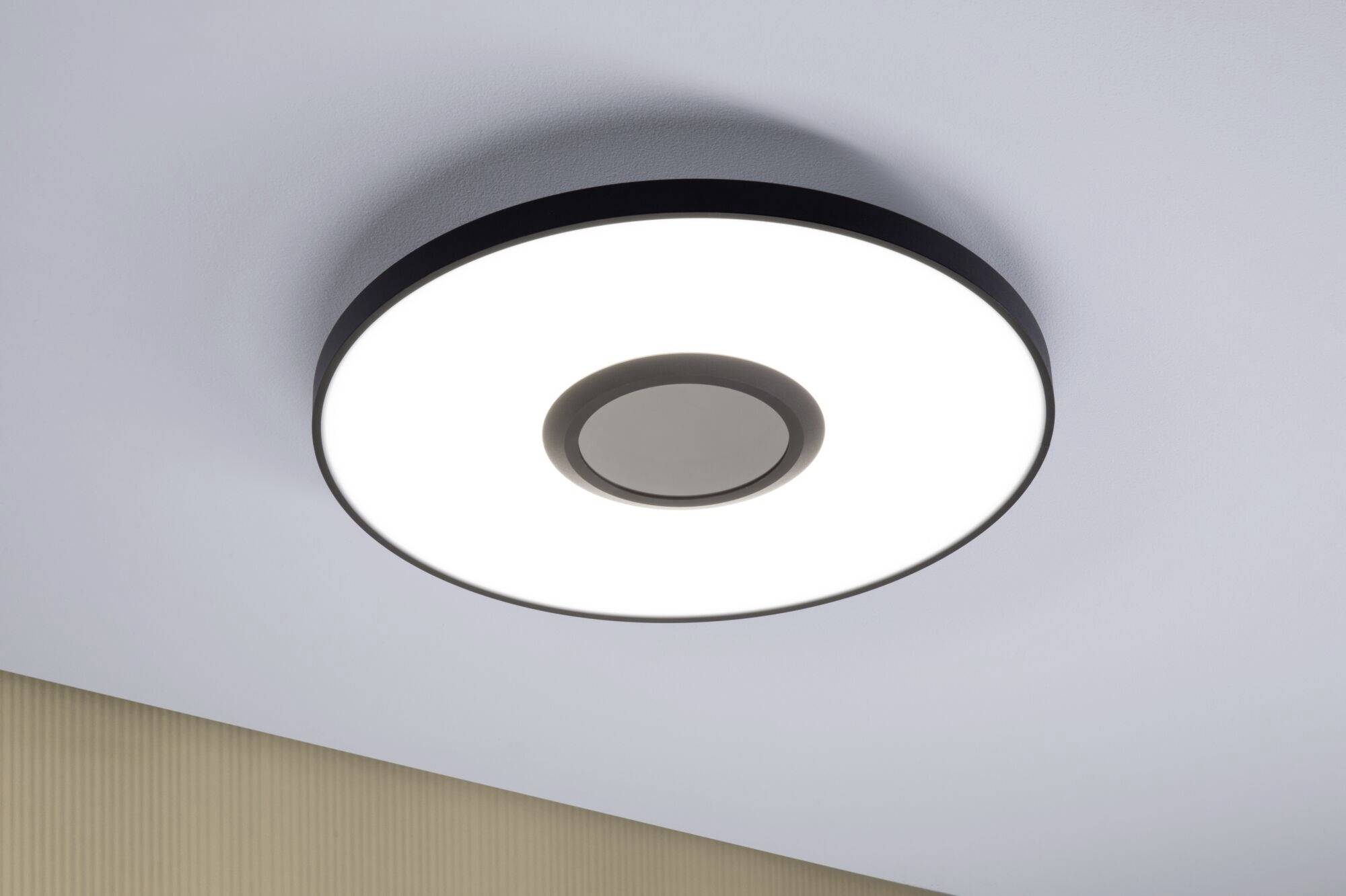 Okrągła, nowoczesna lampa sufitowa z oświetleniem LED, zamontowana na jasnym suficie. Oprawa świeci równomiernie i jasno.