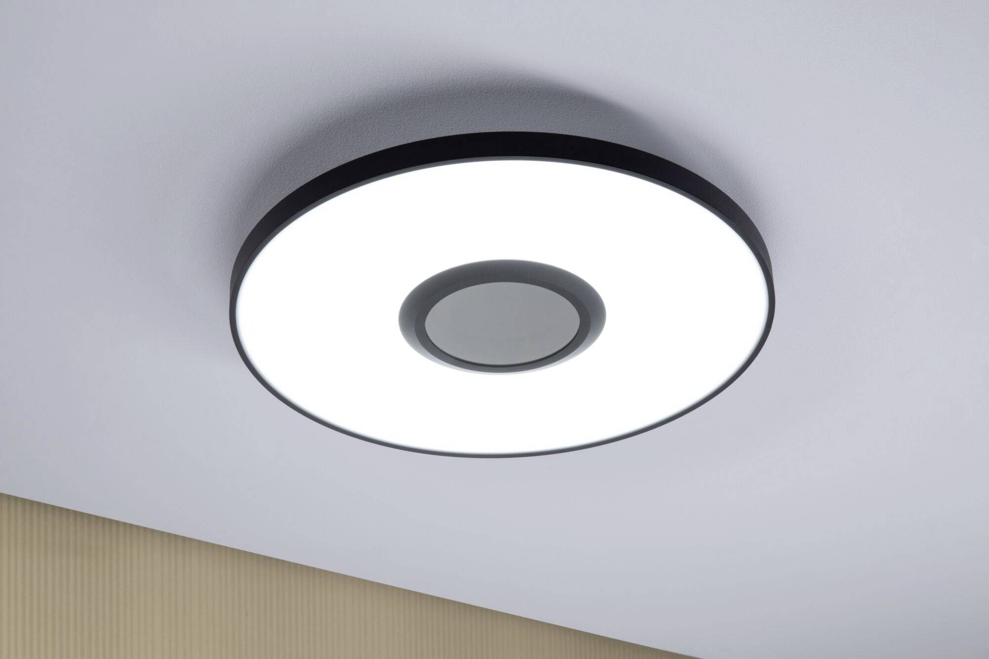 Okrągła, nowoczesna lampa sufitowa emituje jasne białe światło na gładkim suficie we wnętrzu pomieszczenia.