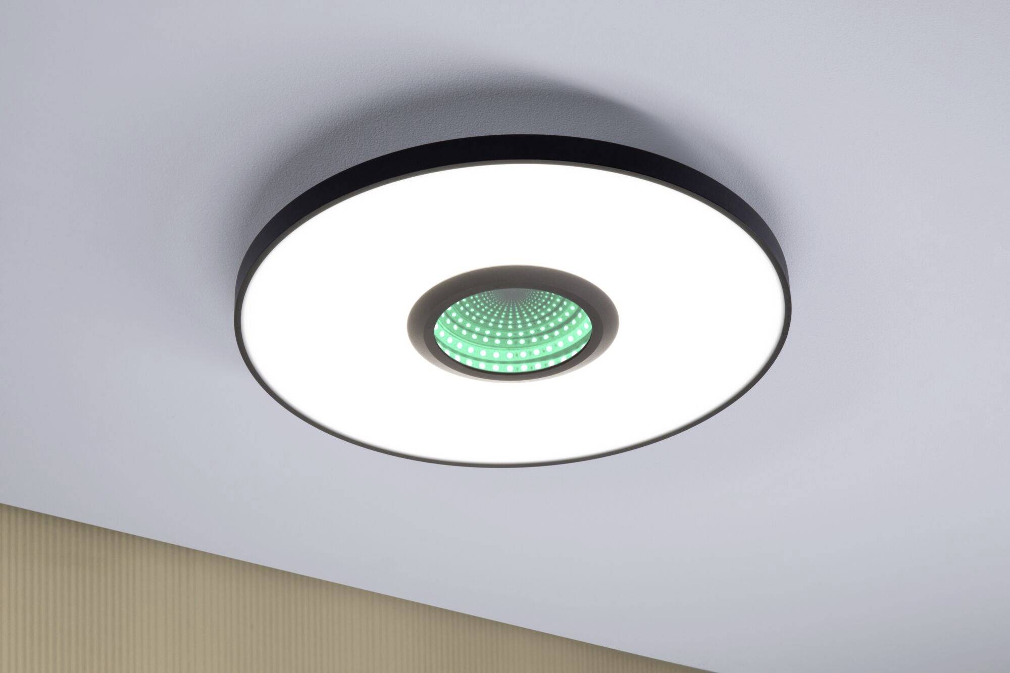 Okrągła lampa sufitowa z centralnym zielonym elementem świetlnym w nowoczesnym pomieszczeniu. Równomiernie oświetla otoczenie.