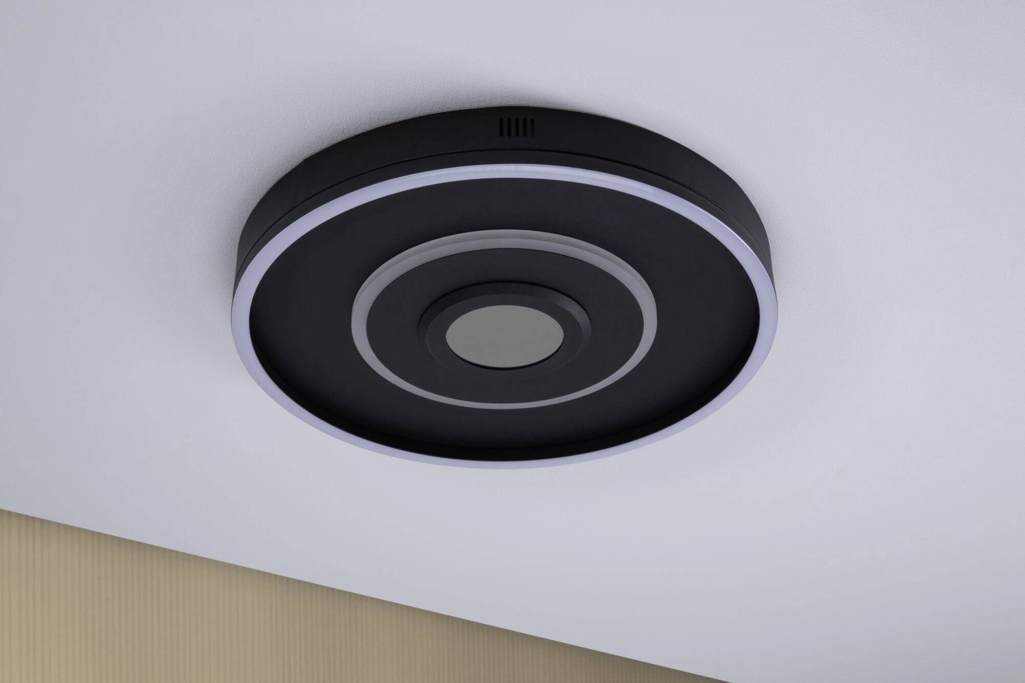 Okrągła czarna lampa sufitowa z białym pierścieniem LED, zamontowana na białym suficie; nowoczesny design, idealnie komponujący się z współczesnymi wnętrzami.