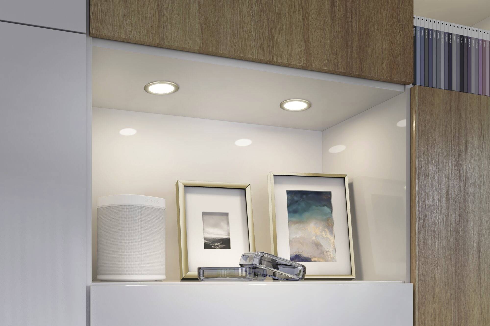 'Dwa oprawione zdjęcia i głośnik na podświetlonej, drewnianej półce, zaprojektowane nowocześnie i minimalistycznie.'