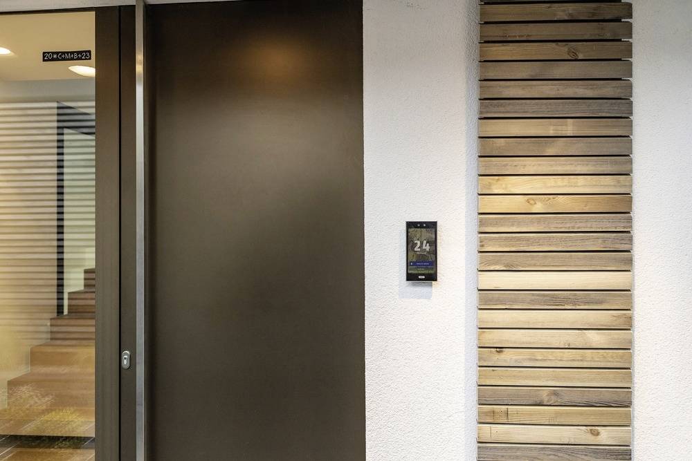 Wejście do nowoczesnego budynku z elementami drewnianymi i drzwiami, oznaczone tabliczką z numerem '24'.