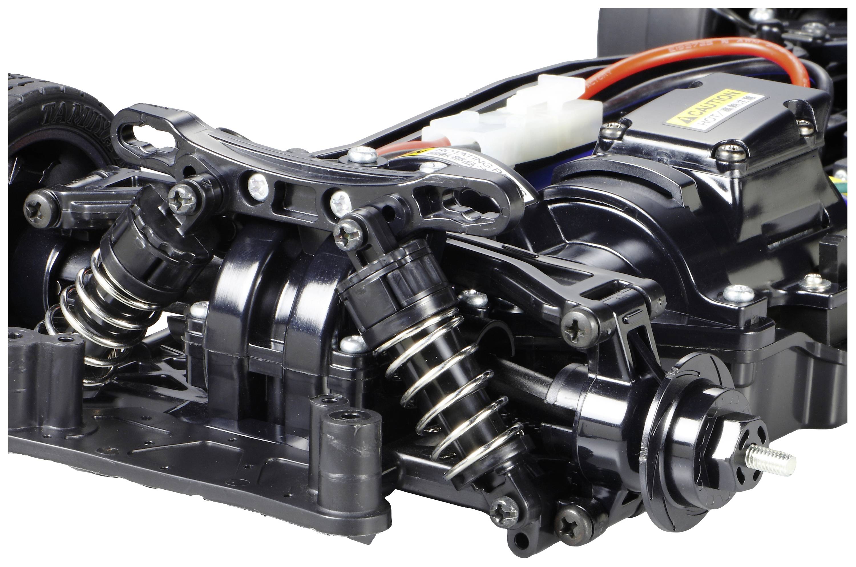 Zbliżenie czarnego podwozia samochodu modelarskiego z amortyzatorami i zawieszeniem. Widoczne szczegóły techniczne i przewody w tle.