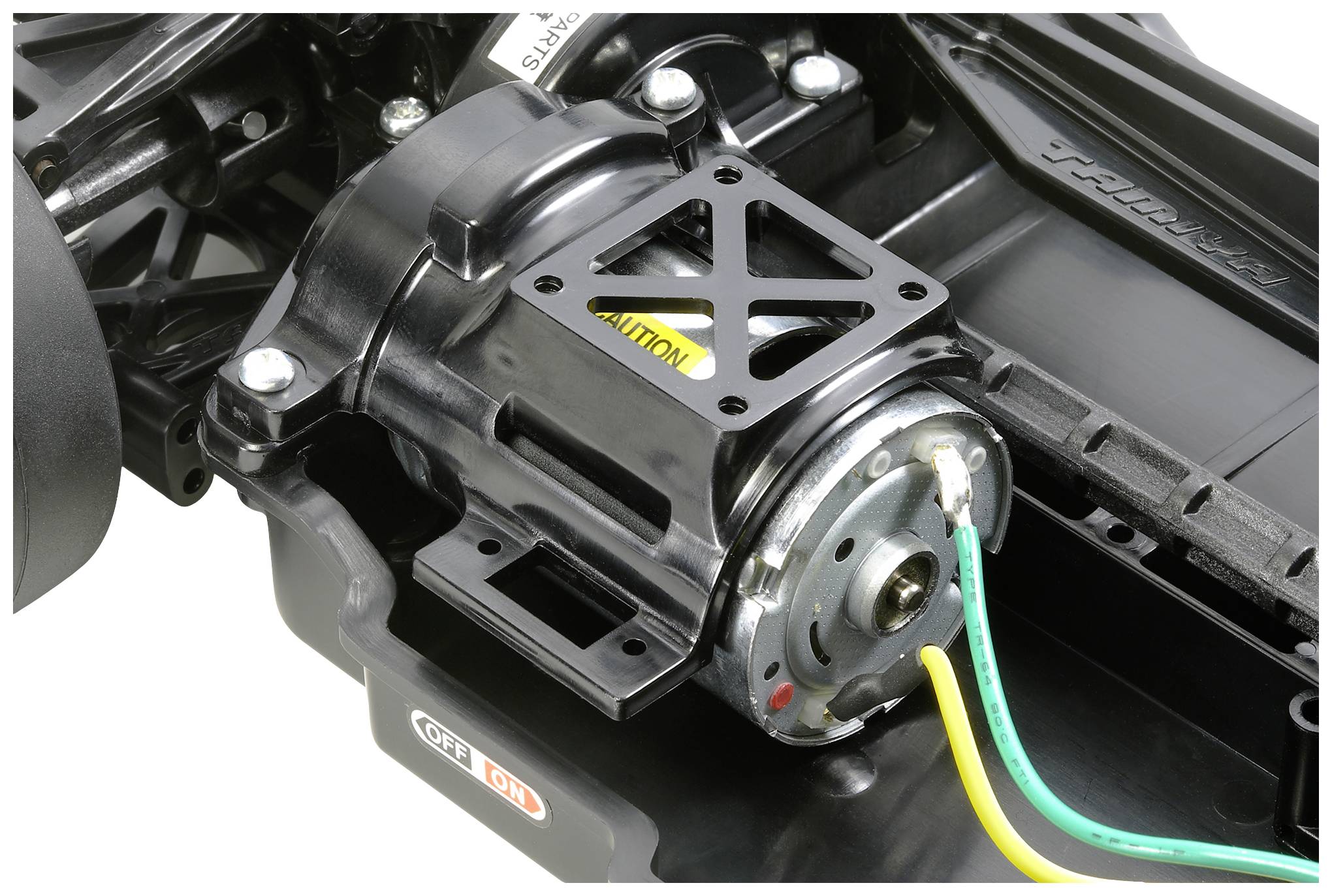 Silnik elektryczny w samochodzie zdalnie sterowanym, z widocznymi zielonymi i żółtymi przewodami, zamontowany w czarnej metalowej obudowie.