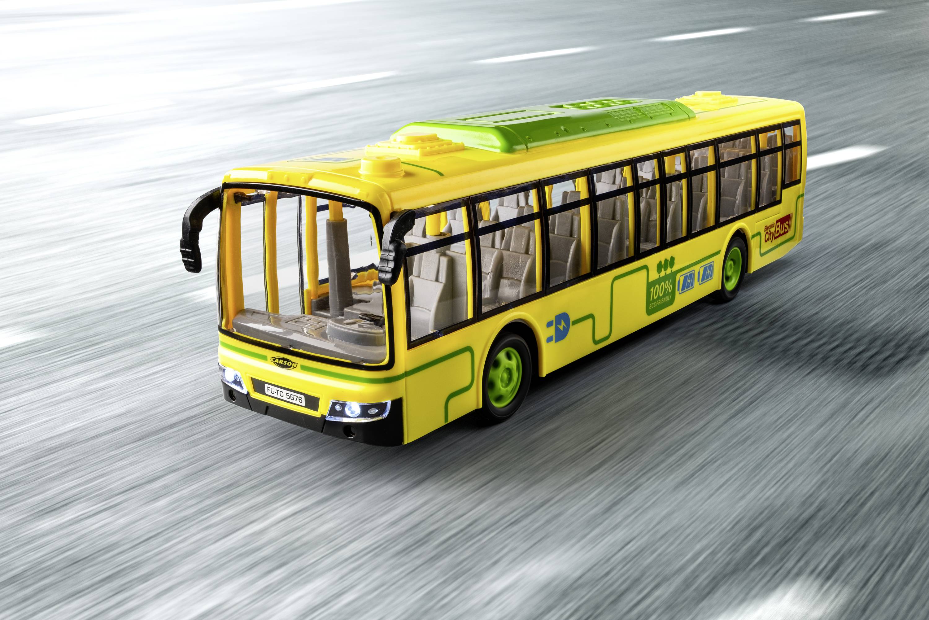 Żółty plastikowy autobus modelowy jedzie po drodze. Autobus ma zielone koła i przezroczyste okna.