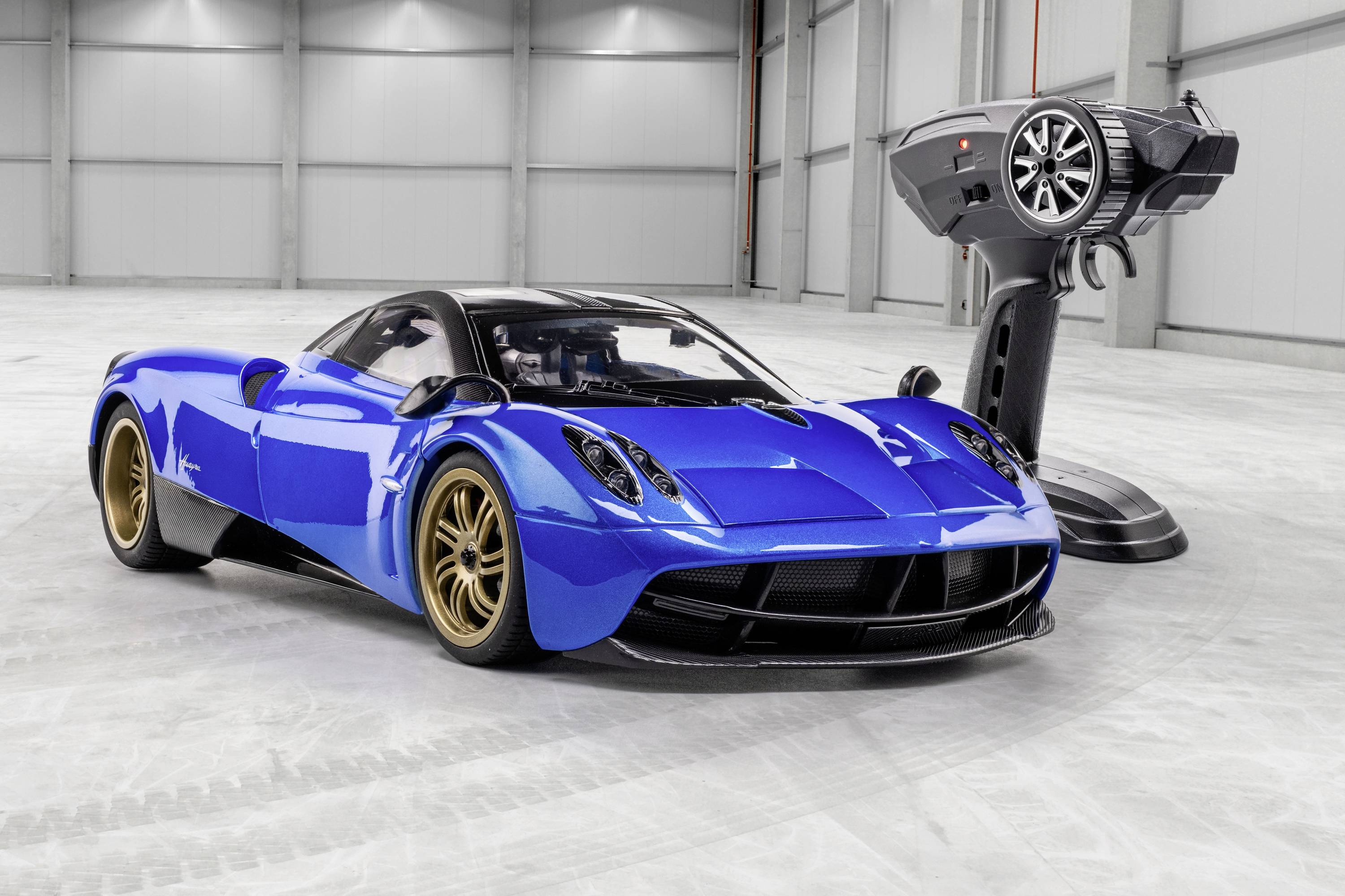 Niebieski samochód sportowy w hali, flankowany przez olbrzymi model samochodu na stojaku.