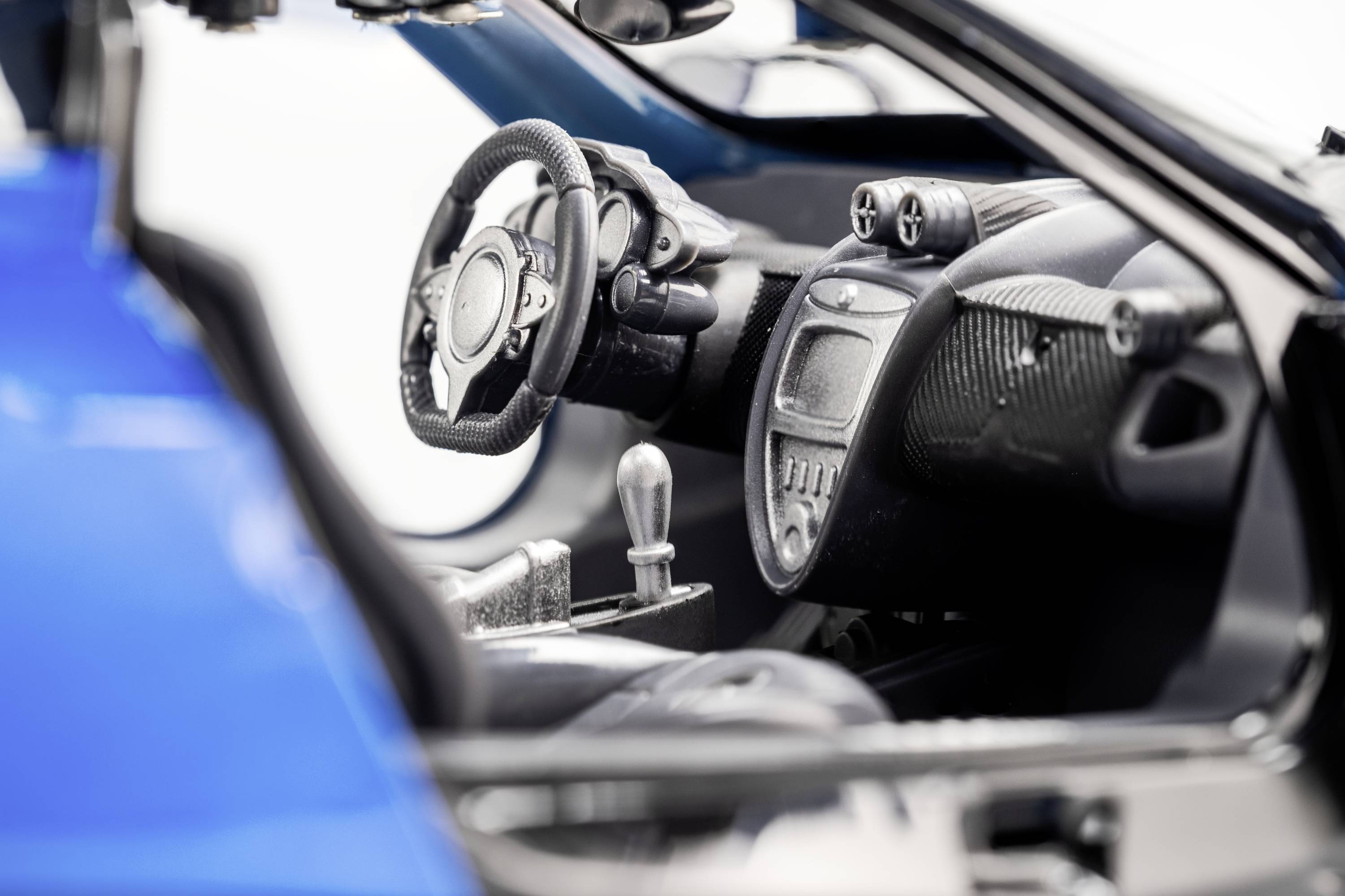 Wnętrze nowoczesnego samochodu z niebieskim nadwoziem przedstawia kierownicę, dźwignię zmiany biegów oraz cyfrowy panel wskaźników.