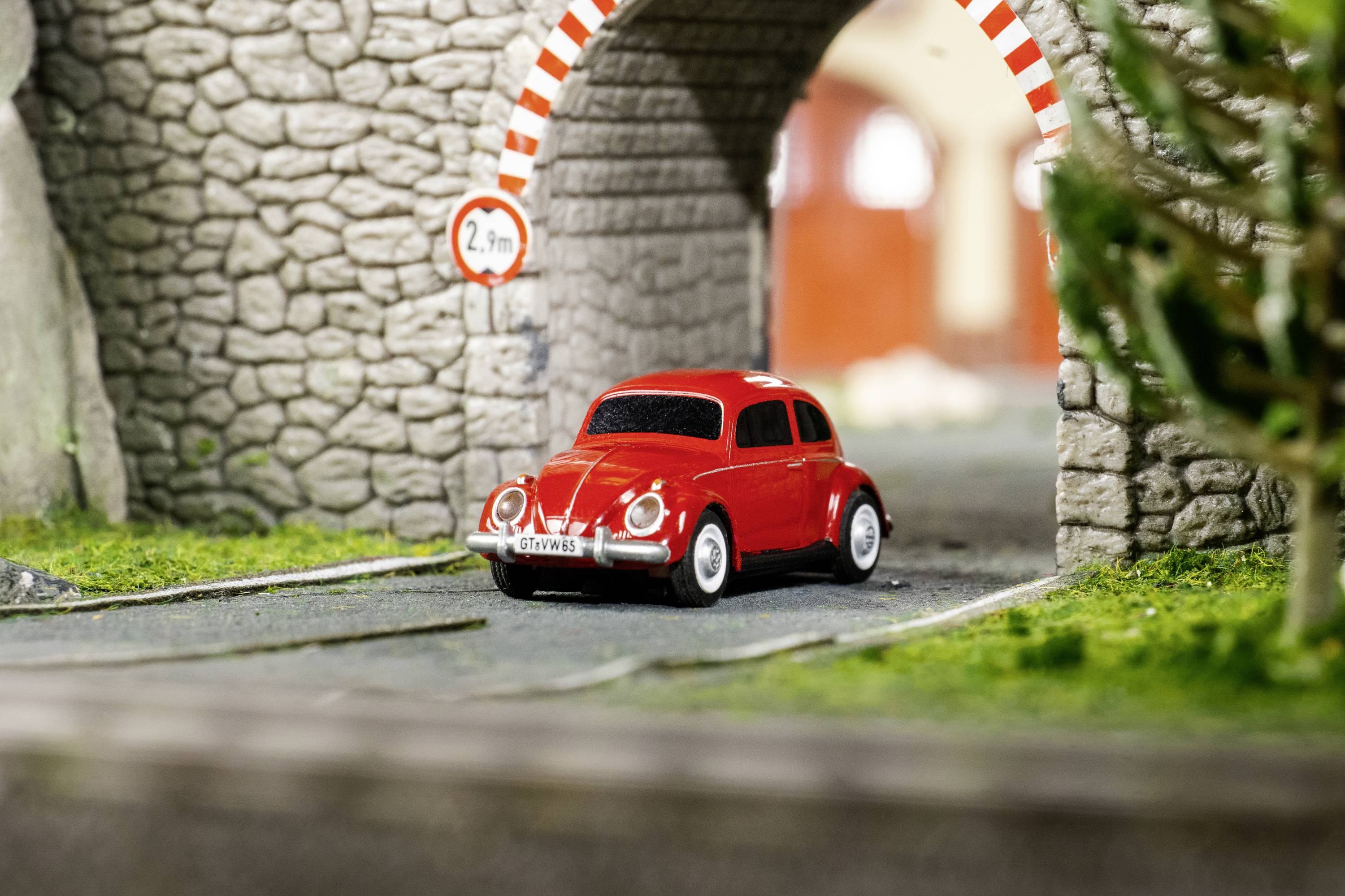Czerwony samochodzik modelarski jedzie przez kamienny tunel o ograniczeniu wysokości 2,7 m.