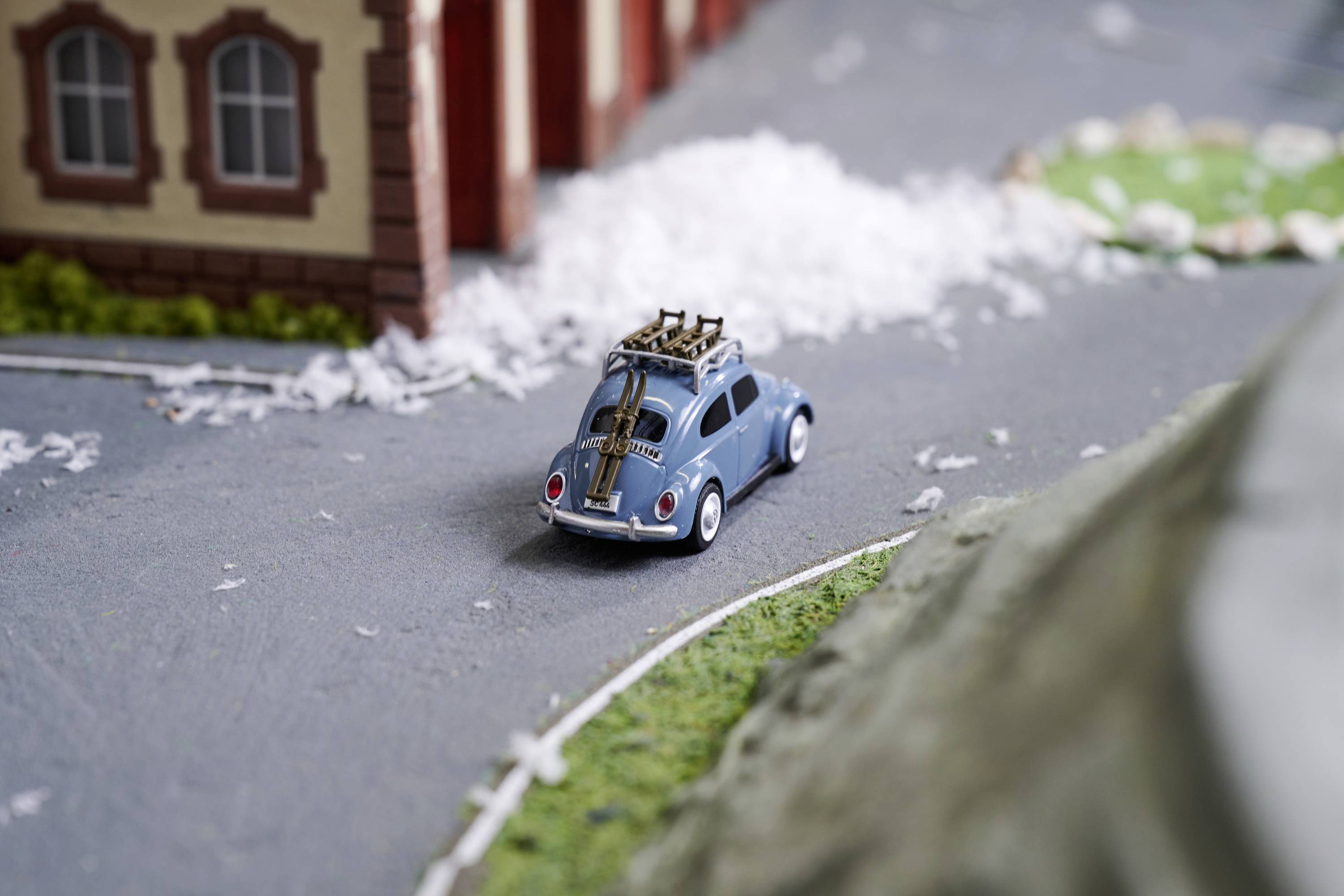 Niebieskie autko modelarskie jedzie po miniaturowej drodze, mijając budynki. Scena jest częścią dokładnie odwzorowanej makiety.