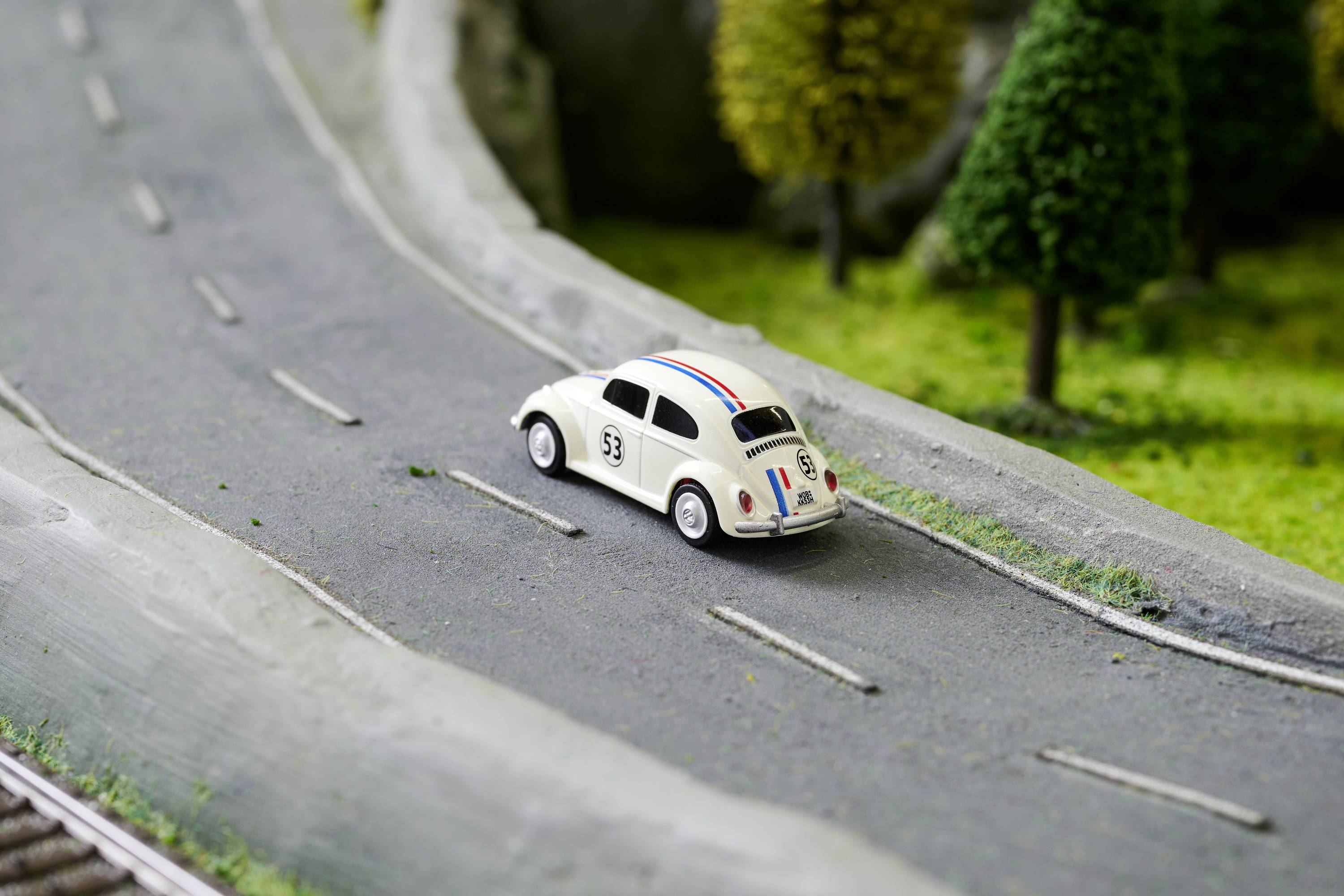 Mały samochodzik modelarski jedzie po miniaturowej drodze przez krajobraz z drzewami w tle.