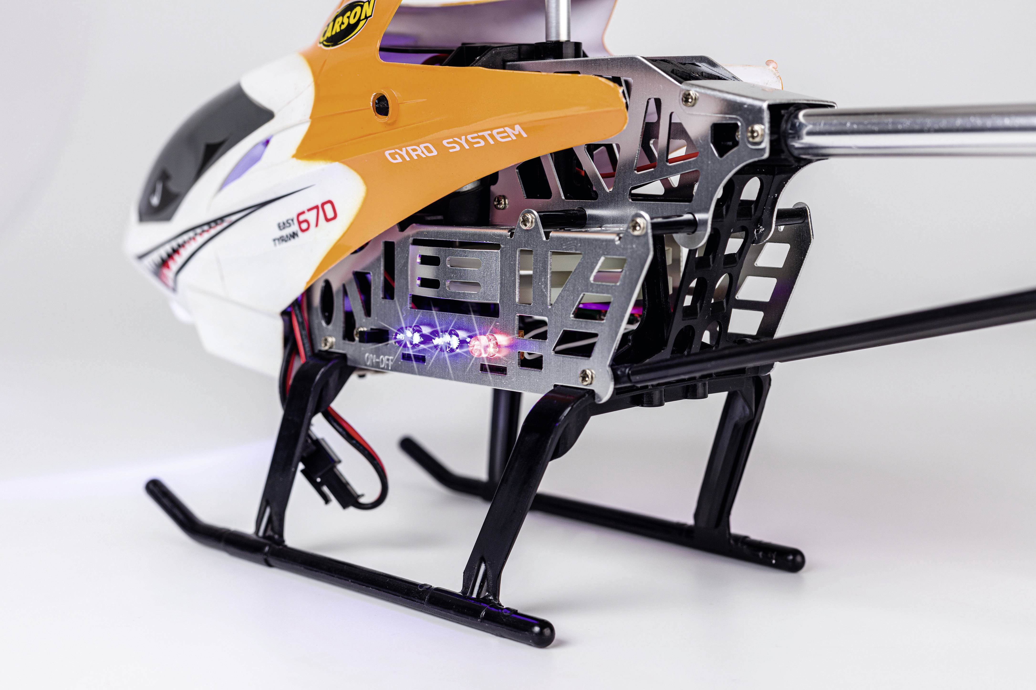 Zdalnie sterowany helikopter w pomarańczowo-białej obudowie, z widocznym napisem 'Gyro System' i widocznymi elementami elektronicznymi.