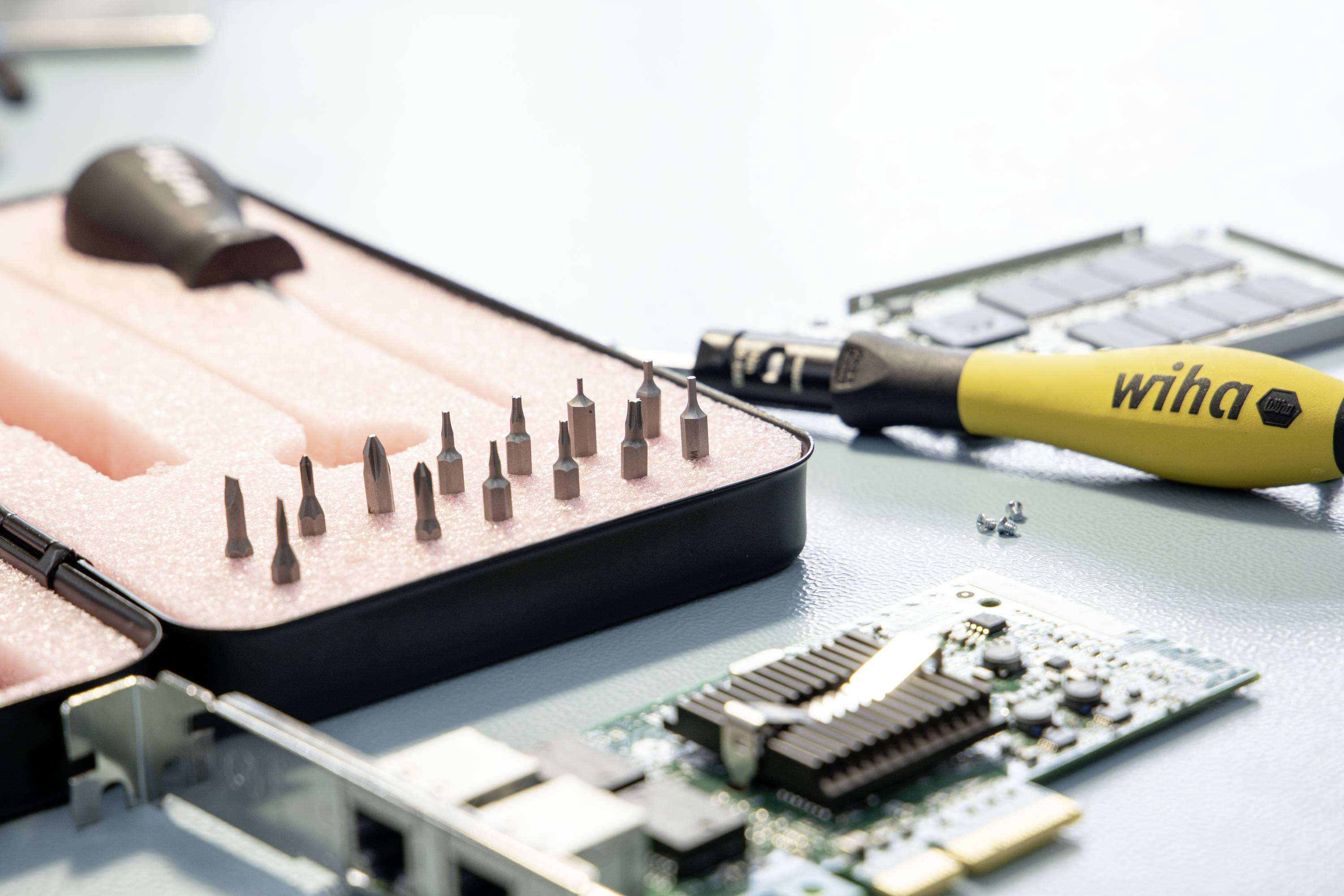 Narzędzia i części sprzętowe na stole. Śrubokręt, zestaw bitów i płyta główna komputera w zbliżeniu.