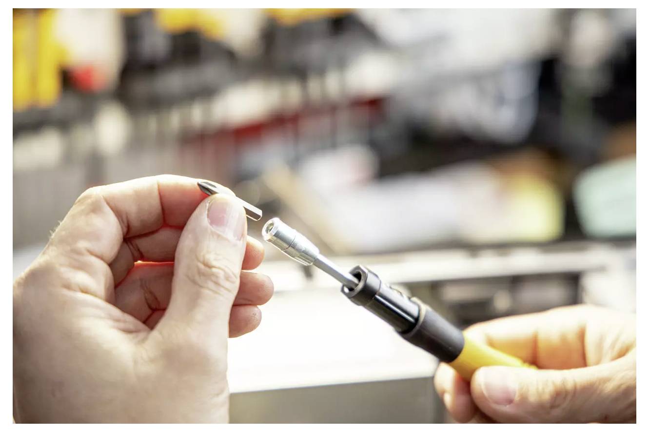 Osoba trzyma lutownicę z małym metalowym komponentem, co wskazuje na trwającą precyzyjną pracę inżynieryjną lub naprawę urządzeń elektronicznych.