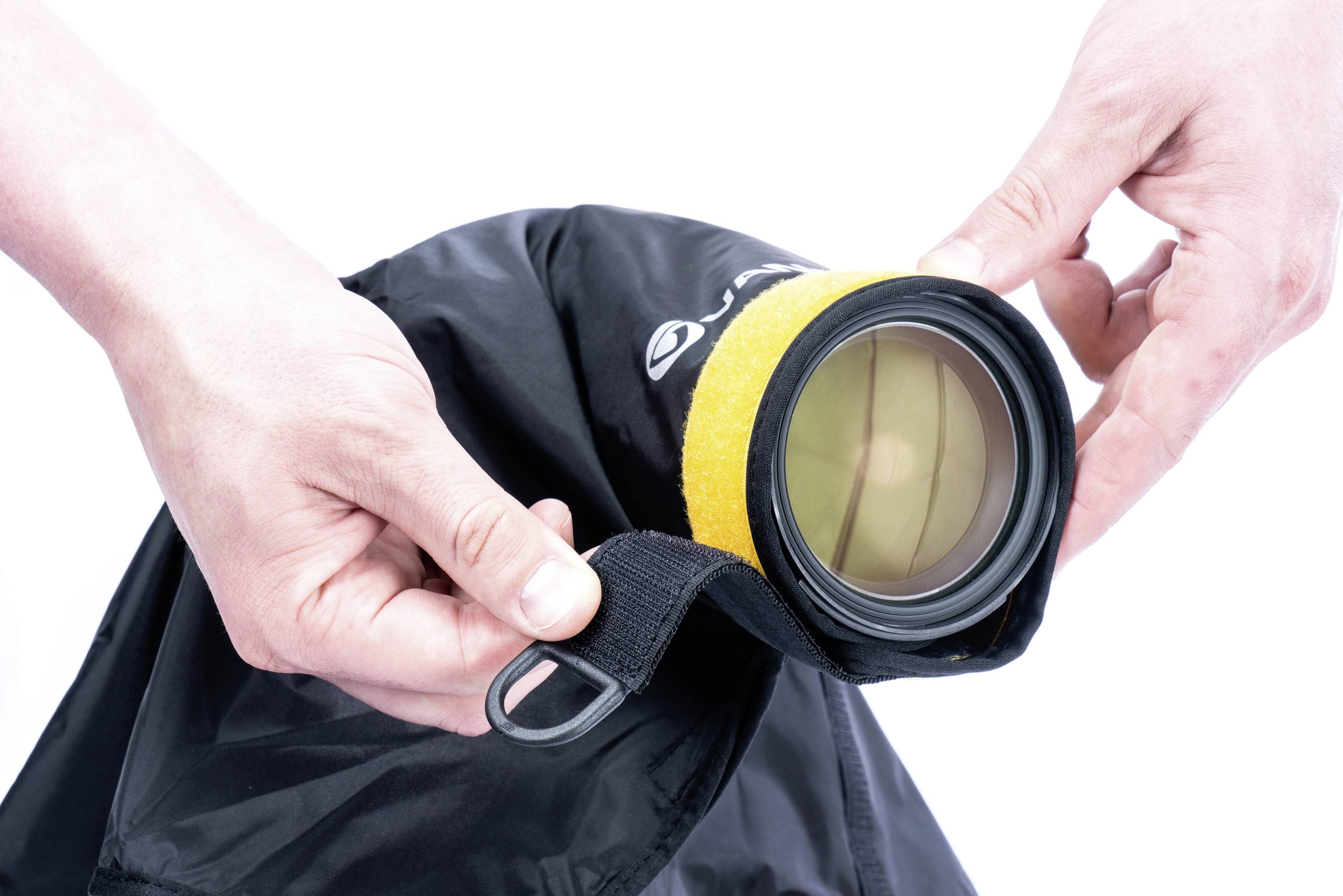 Ręce trzymają aparat z żółtą osłoną obiektywu, otoczony czarną tkaniną, która zabezpiecza kamerę przed warunkami atmosferycznymi.