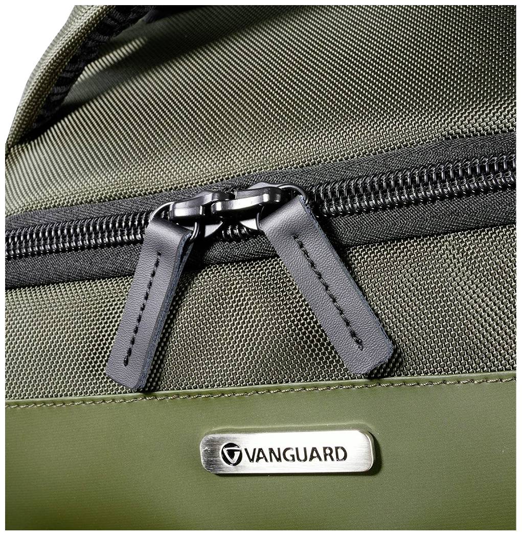 Zielony plecak w szczegółach, prezentujący zamek błyskawiczny i logo 'Vanguard' na metalowej tabliczce.