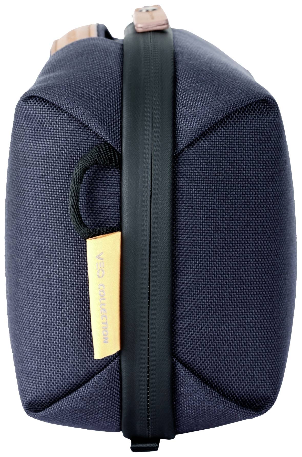 Ciemnoniebieska, prostokątna torba z czarnym zamkiem błyskawicznym i brązowym uchwytem. Po jednej ze stron umieszczona jest etykieta z napisem.