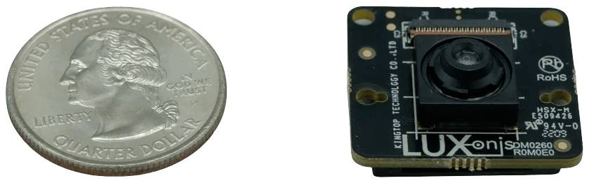 'Moneta obok małej kamery na czarnej płytce z napisem 'Luxonis'. Przedstawia porównanie wielkości między monetą a kamerą.'