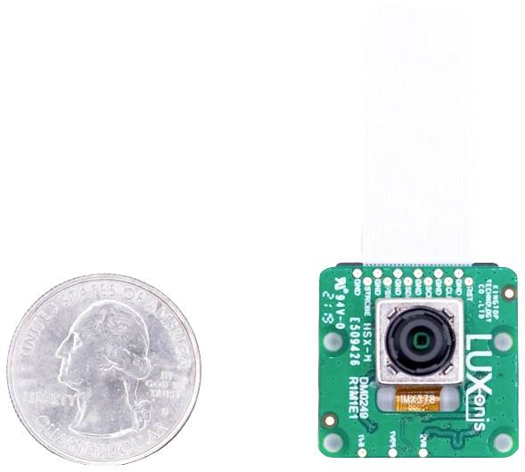 Mała zielona płytka kamery z obiektywem, umieszczona obok monety quarter dolara, ilustrująca proporcje wielkości.