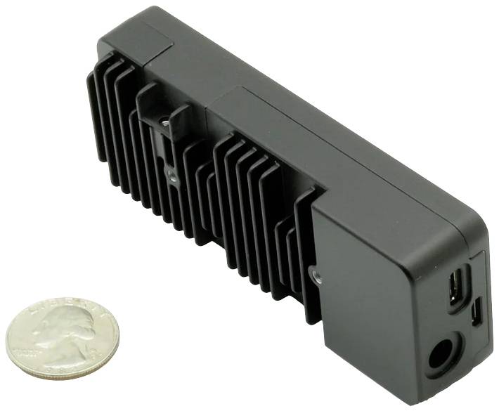 Czarny, prostokątny radiator obok monety jako odniesienie wielkości. Posiada złącza dla urządzeń elektronicznych.