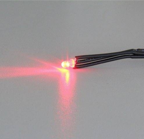 Czerwona dioda LED jasno świeci na ciemnym przewodzie. Emituje światło w lewo, tworząc poświatę na powierzchni.