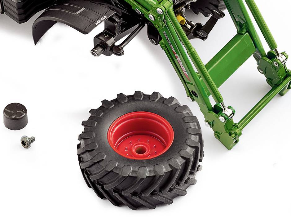 Zielony traktor w trakcie montażu z zamontowanymi przednimi kołami. Opony i śruba leżą obok po lewej stronie.