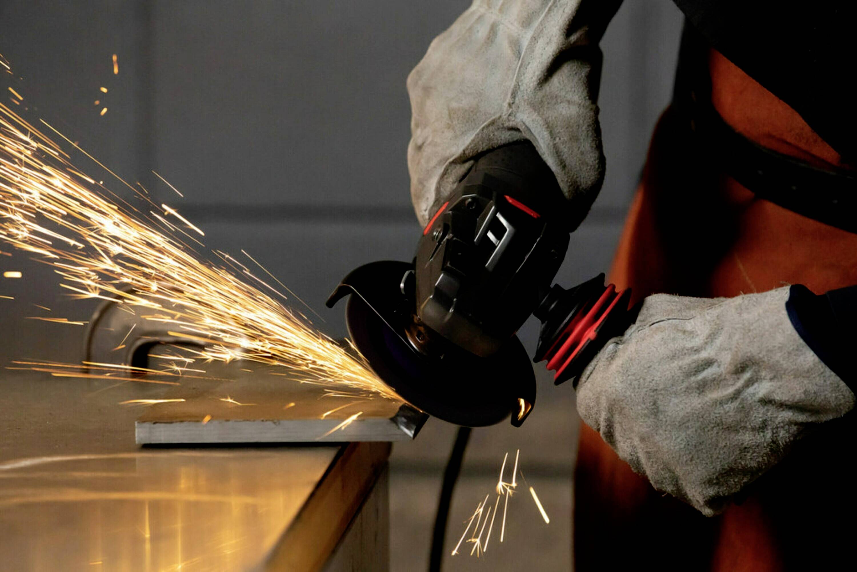Osoba szlifuje metal kątrówką. Iskry lecą w różnych kierunkach. Nosi rękawice ochronne.