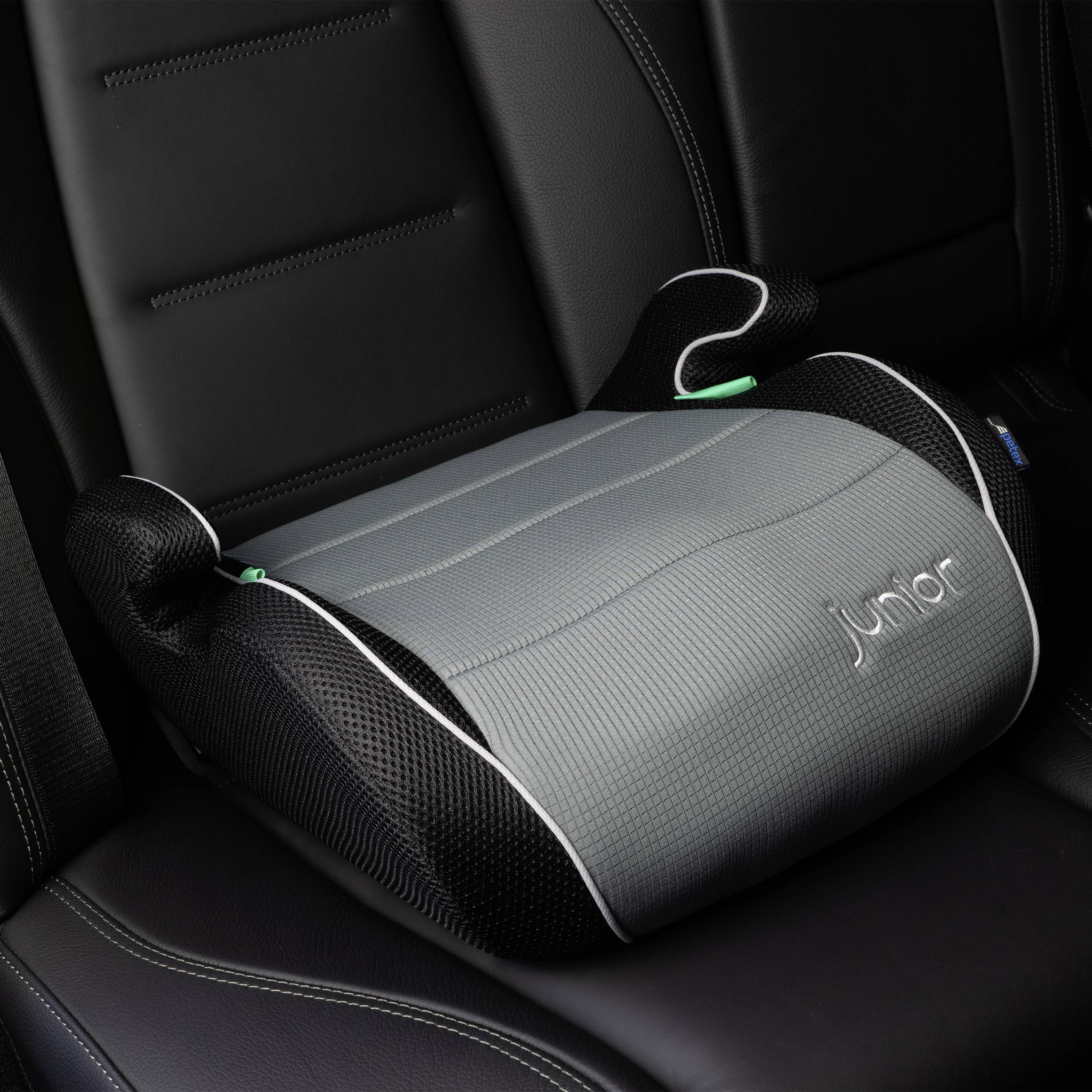 Szara podwyższona fotelik dziecięcy z czarnymi bokami spoczywa na siedzeniu samochodowym. Widoczny jest napis 'junior'.
