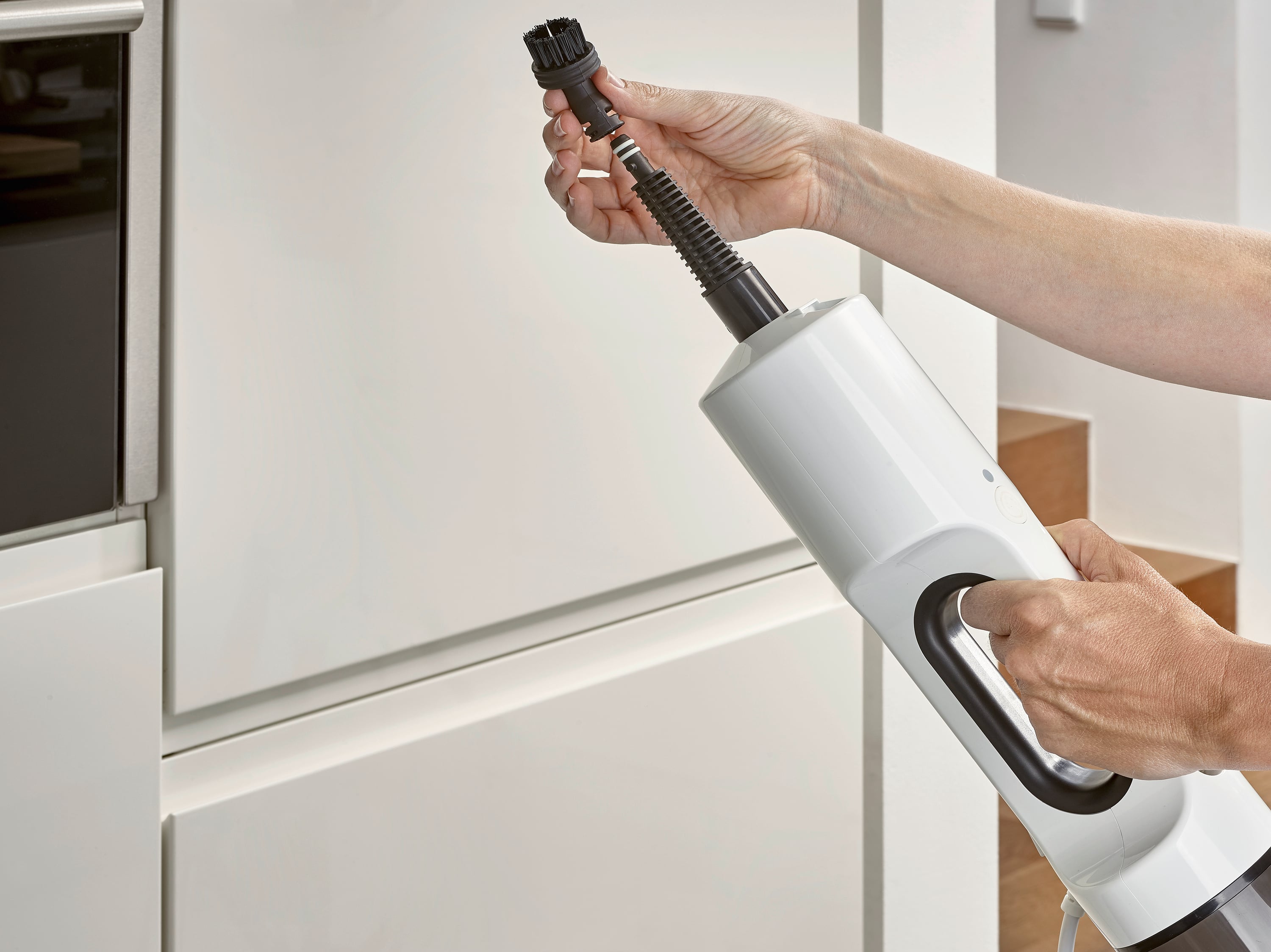 Osoba trzyma odkurzacz i mocuje końcówkę szczotkową. W tle widać szafki kuchenne.