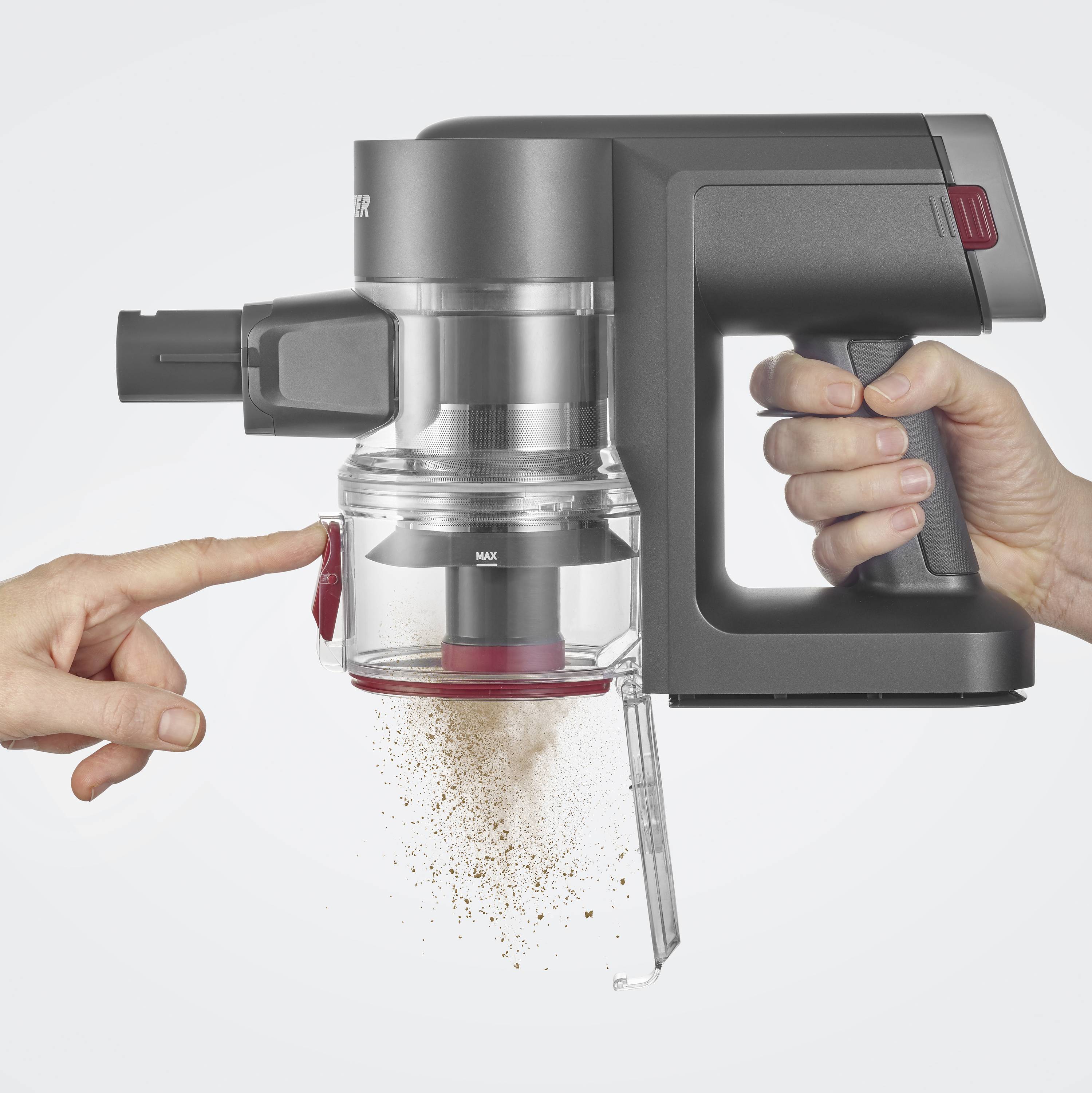 Odkurzacz jest trzymany, a brud wysypuje się z otwartego pojemnika. Ręka wskazuje na proces opróżniania.