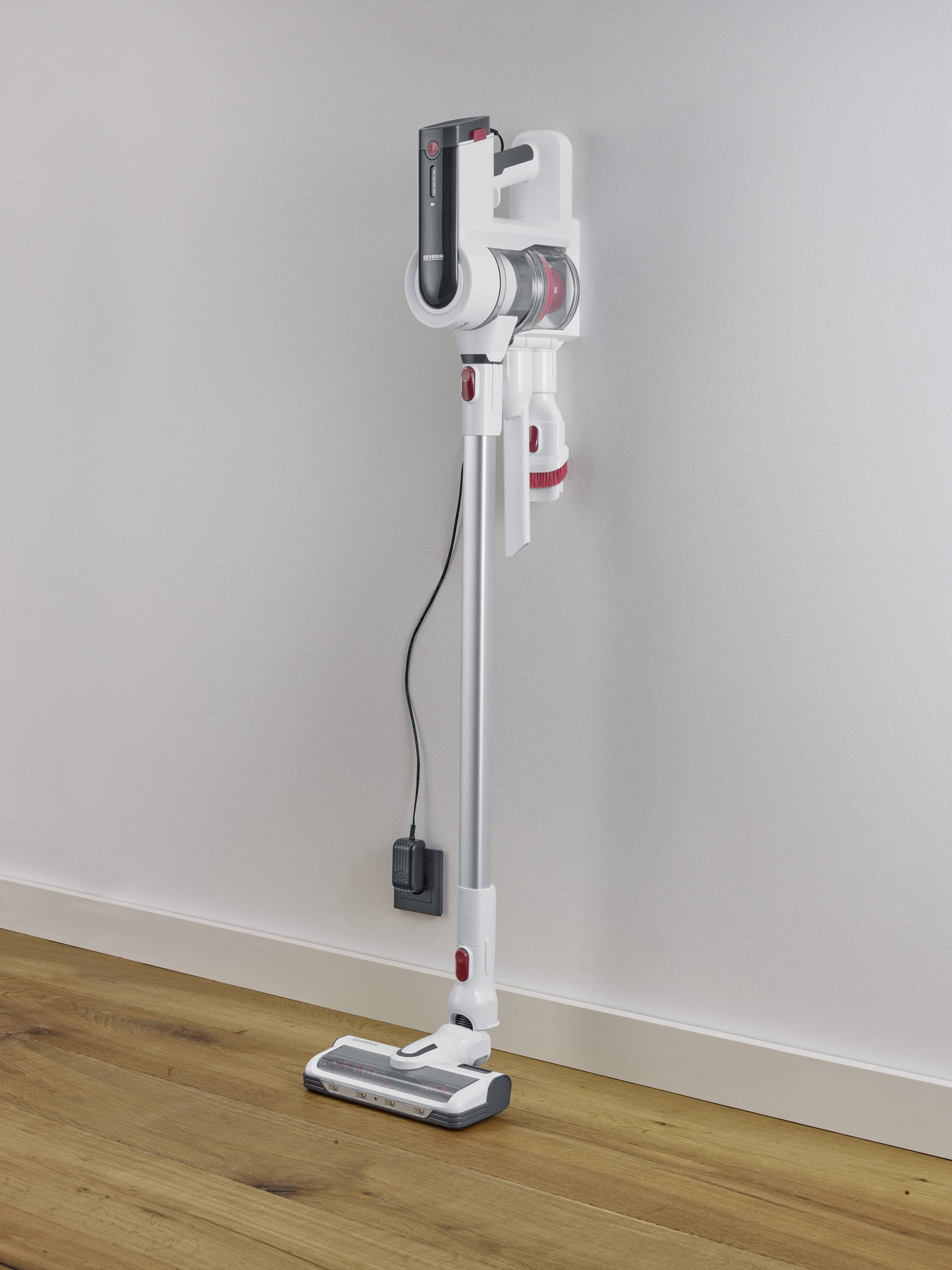 Bezprzewodowy, biały odkurzacz stoi pionowo przy ścianie, z zamocowaną stacją ładującą z boku. Idealny do nowoczesnych gospodarstw domowych.