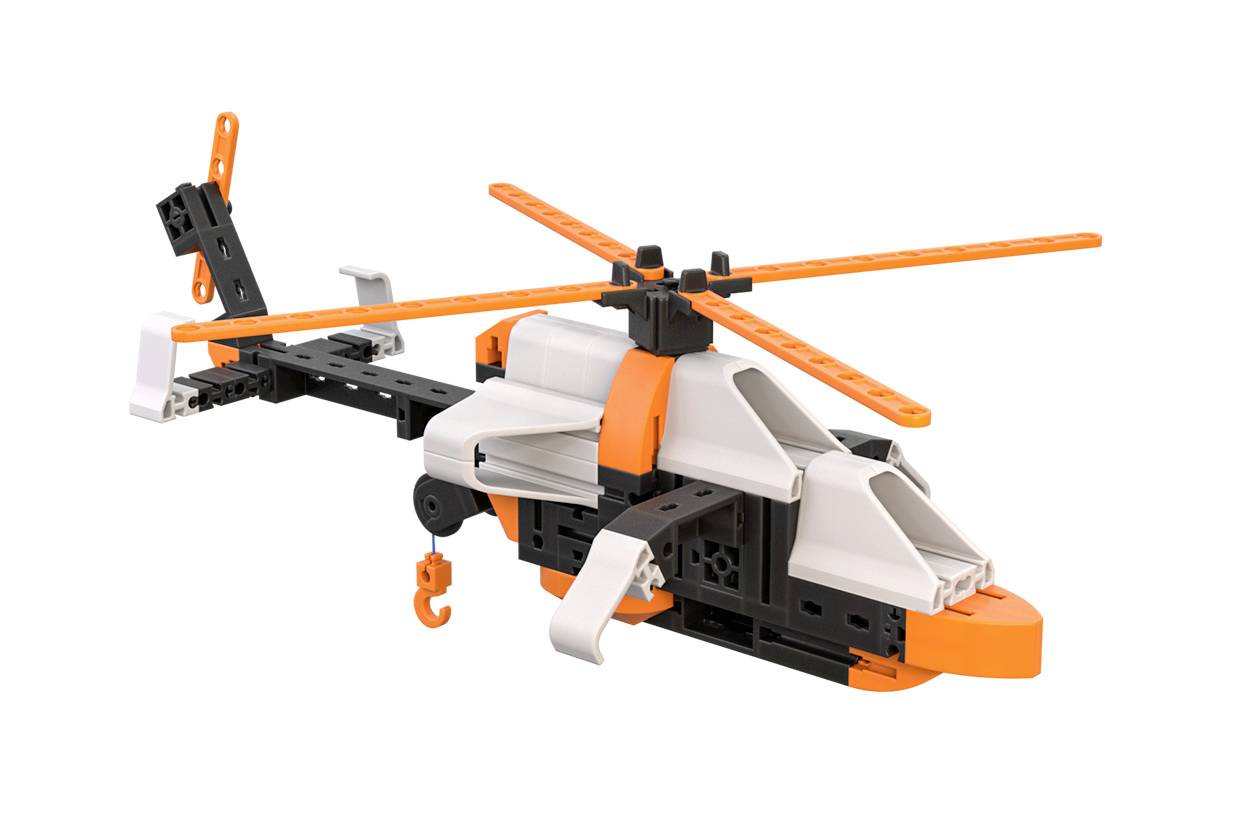 Miniaturowy helikopter z czarnych i białych klocków z pomarańczowymi łopatami wirnika i hakiem unosi się w powietrzu.