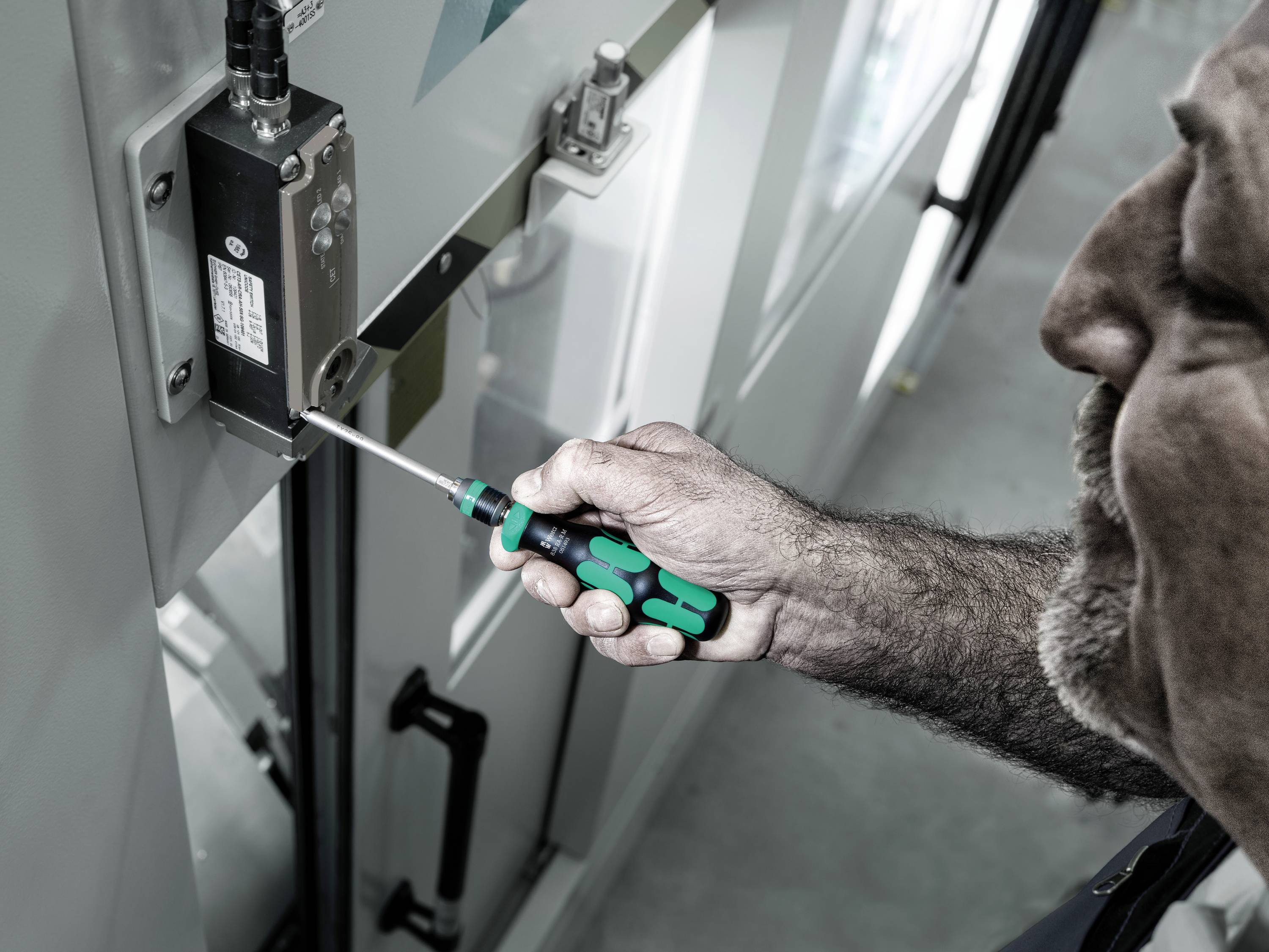 Mężczyzna naprawia maszynę śrubokrętem. Zbliżenie ukazuje precyzyjną czynność wykonywaną przy podzespole elektronicznym.