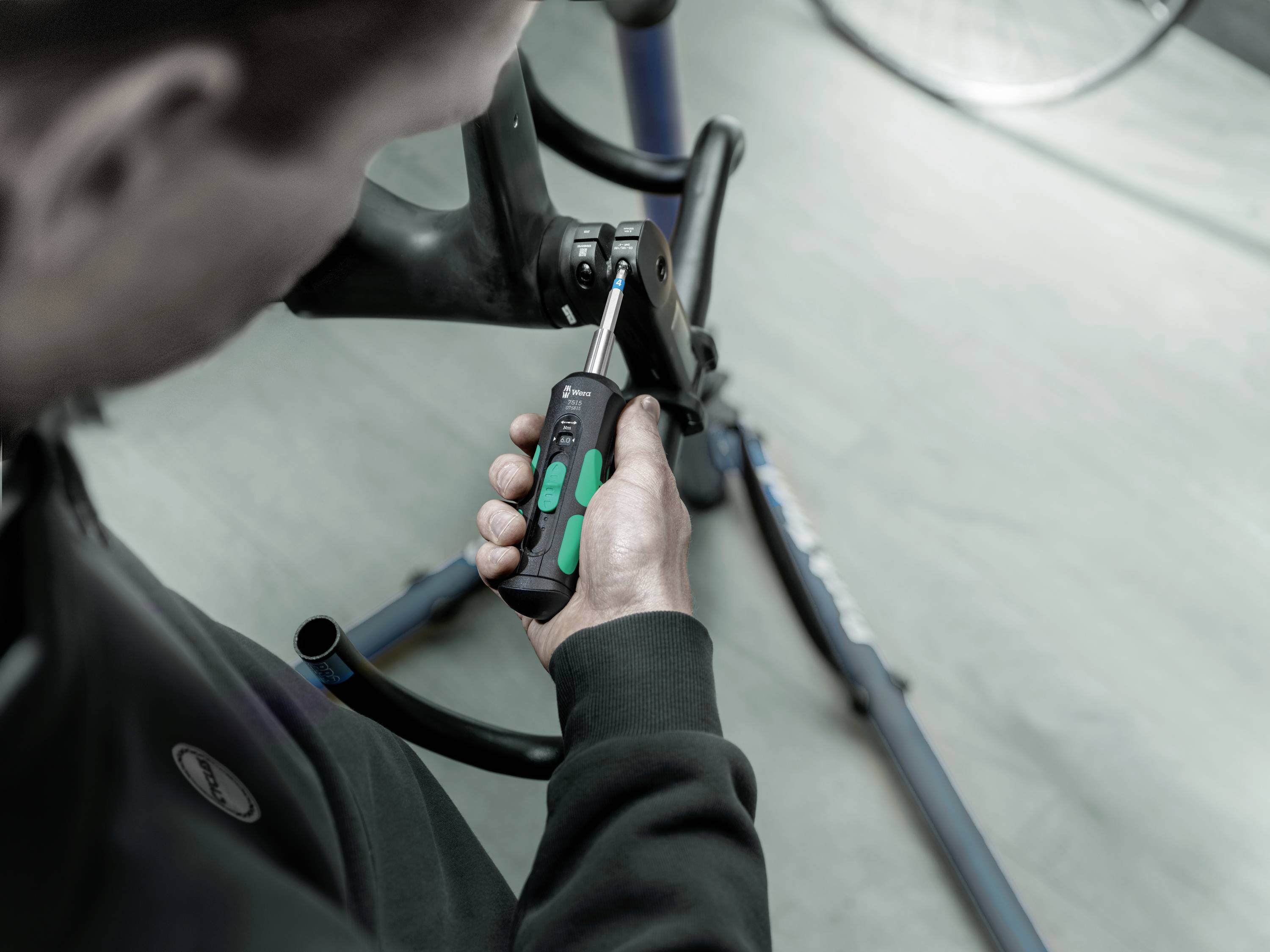 Osoba naprawia ramę rowerową na stojaku, używając śrubokręta w warsztacie.