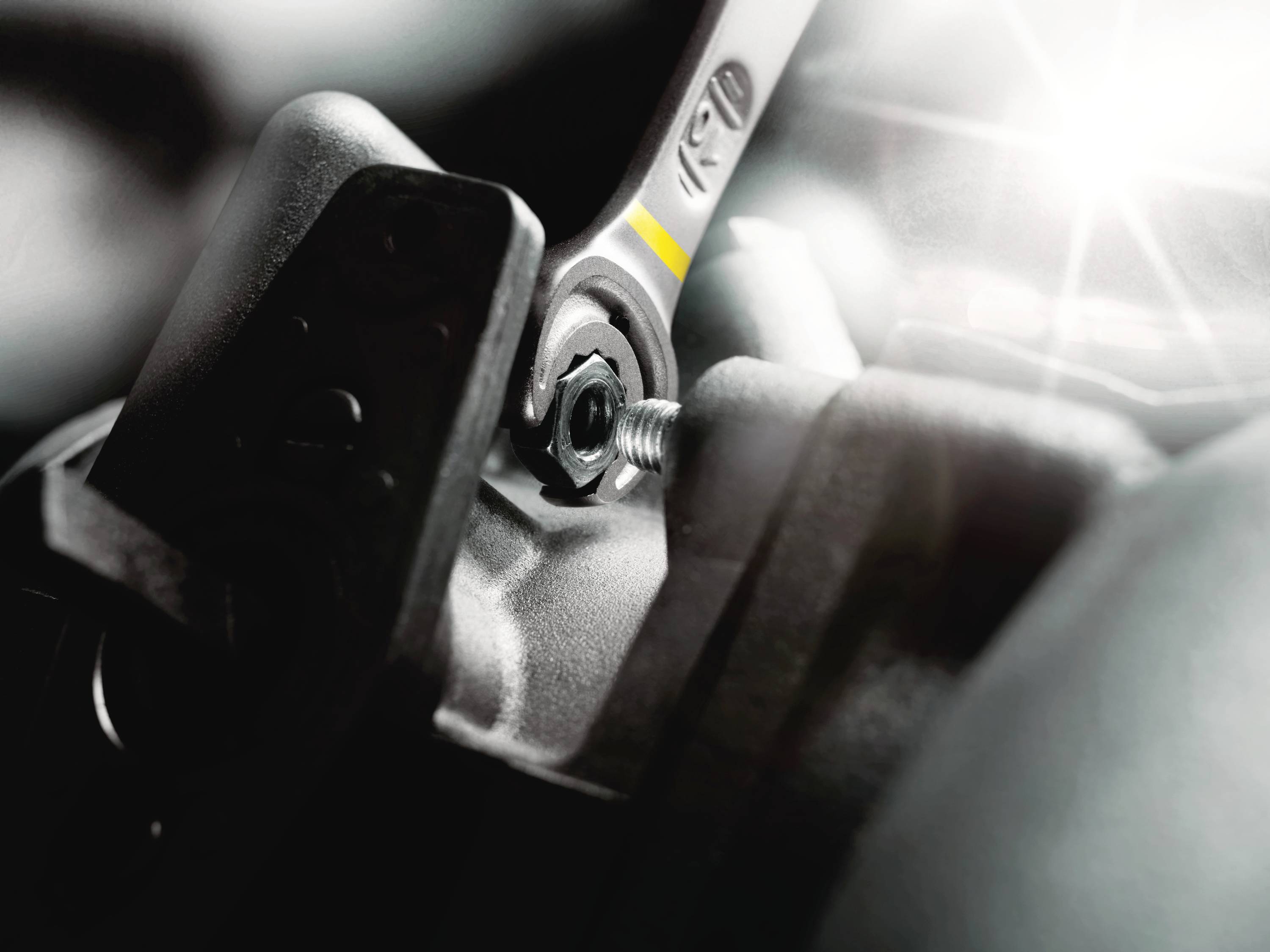 Klucz nakrętkowy dokręca śrubę na elemencie metalowym, podczas gdy wiązki światła zapewniają dodatkowe oświetlenie.