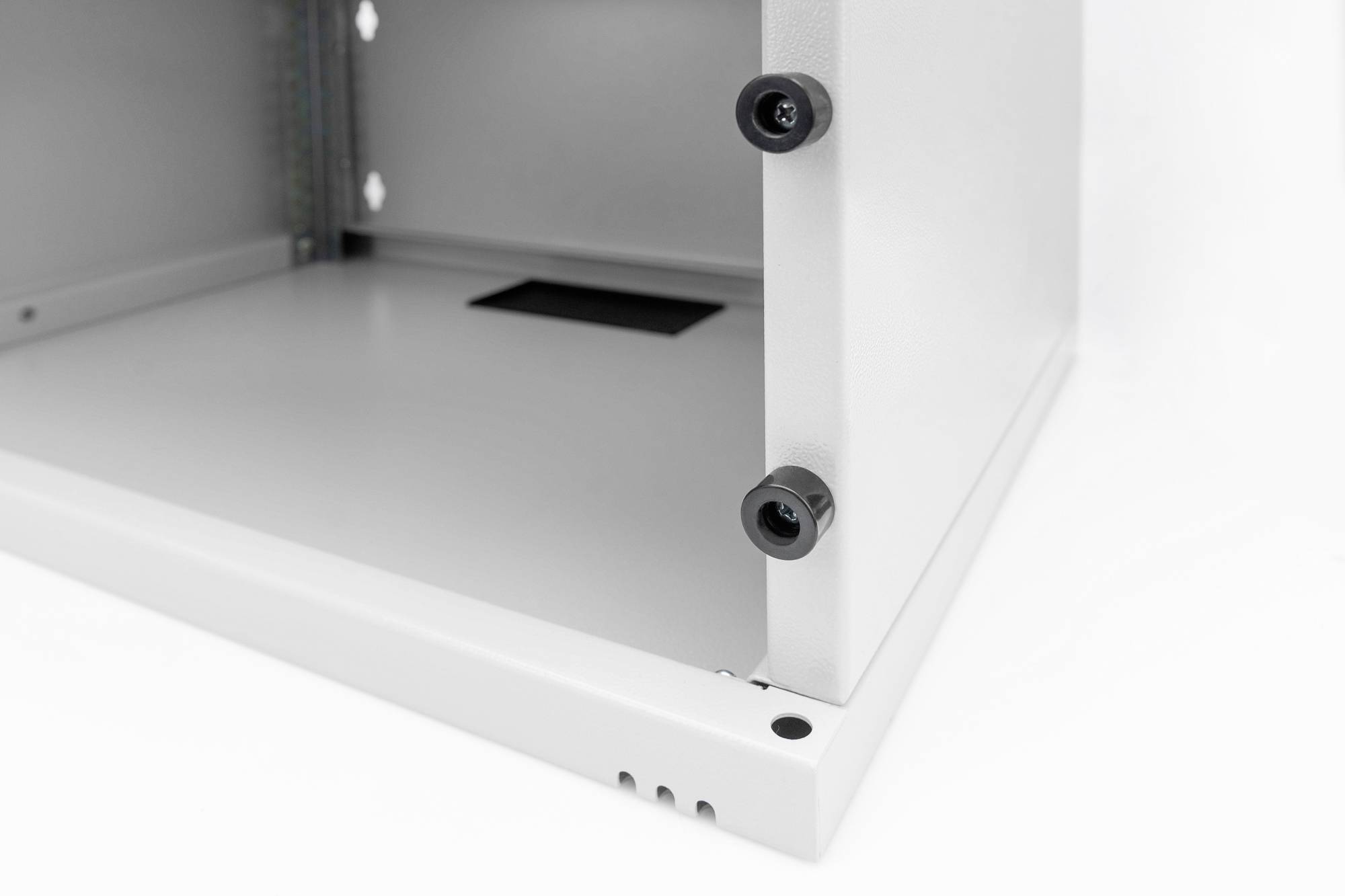 Widok z boku białej metalowej szafki z widocznymi śrubami i otworami wentylacyjnymi, częściowy wgląd w strukturę wewnętrzną.