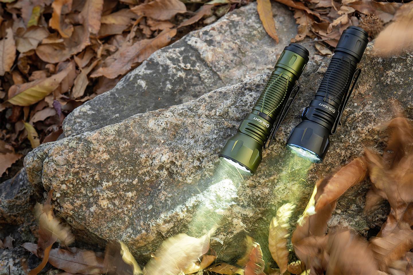 Dwie latarki świecą na skale, otoczone jesiennymi liśćmi. Jedna jest oliwkowozielona, druga czarna.