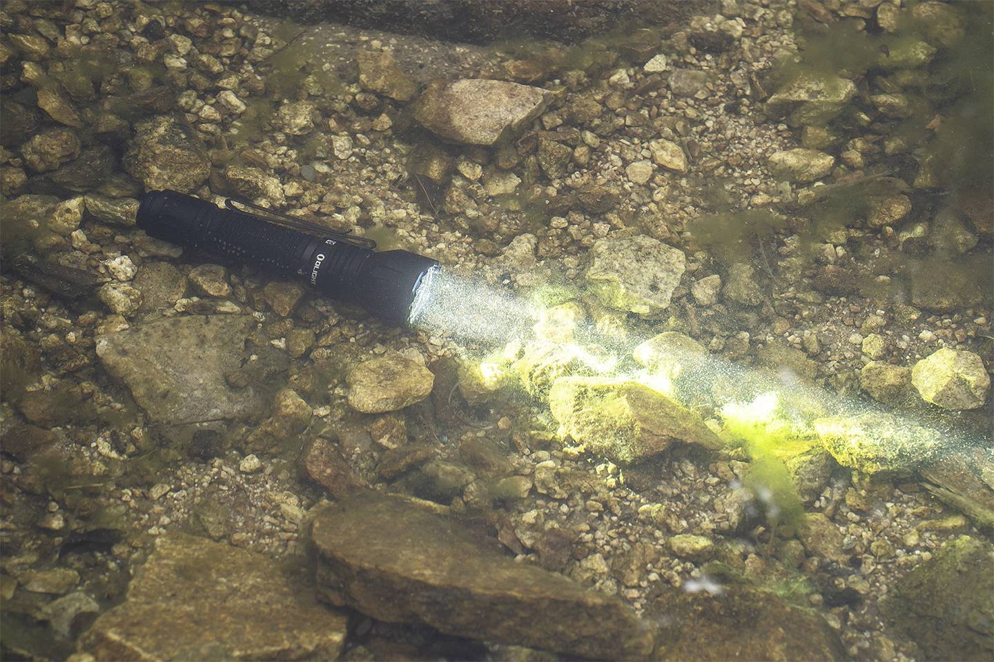 Latarka pod wodą, której wiązka światła pada na kamieniste dno.