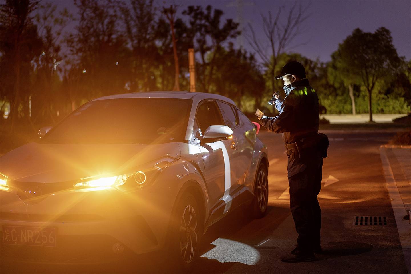 Policjant kontroluje zatrzymany samochód na nocnej drodze. Reflektor samochodu świeci jasnym światłem.