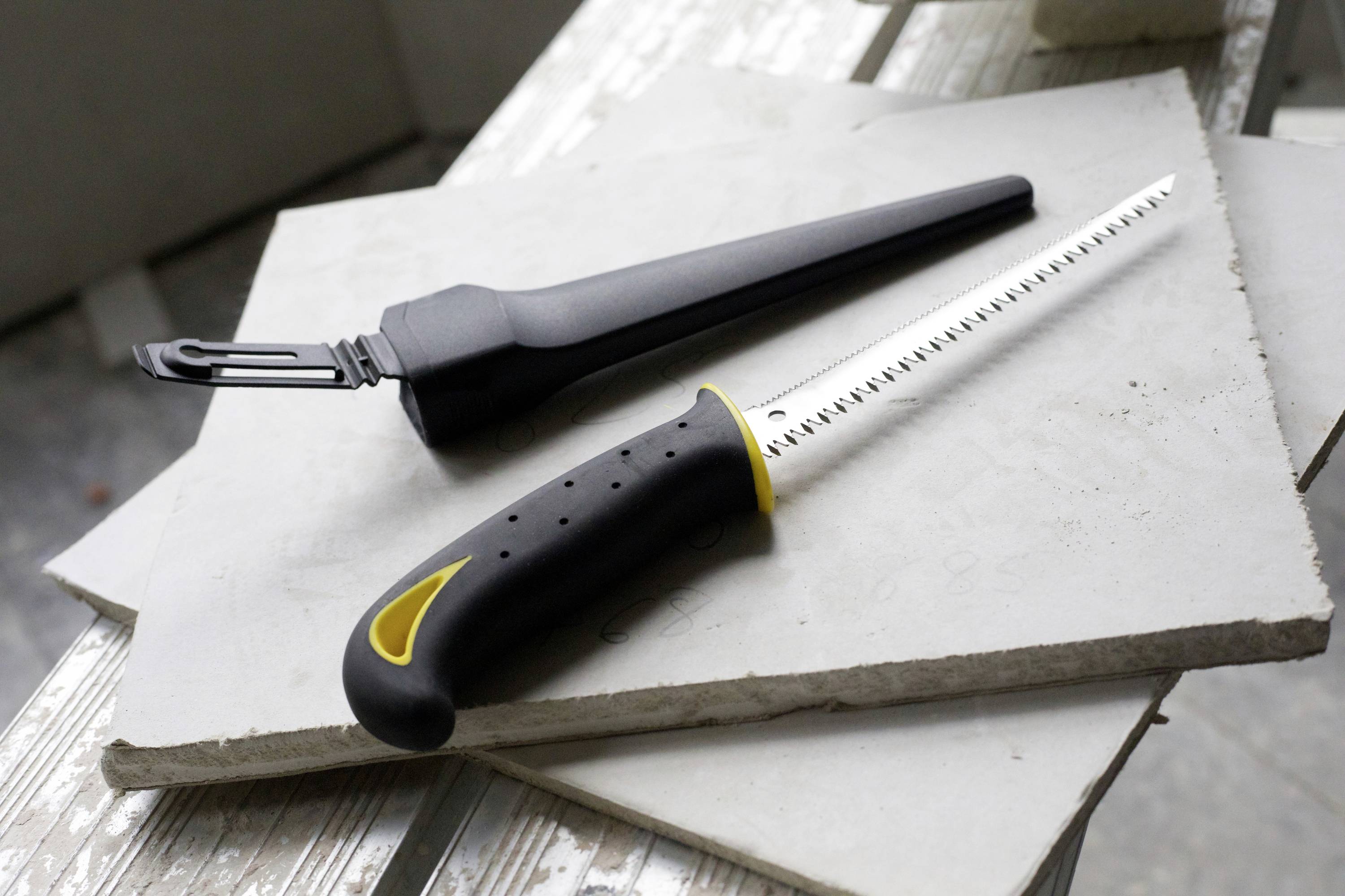 Piła do cięcia płytek leży na stosach płytek. Obok znajduje się osłona ochronna piły. Środowisko pracy w budownictwie.