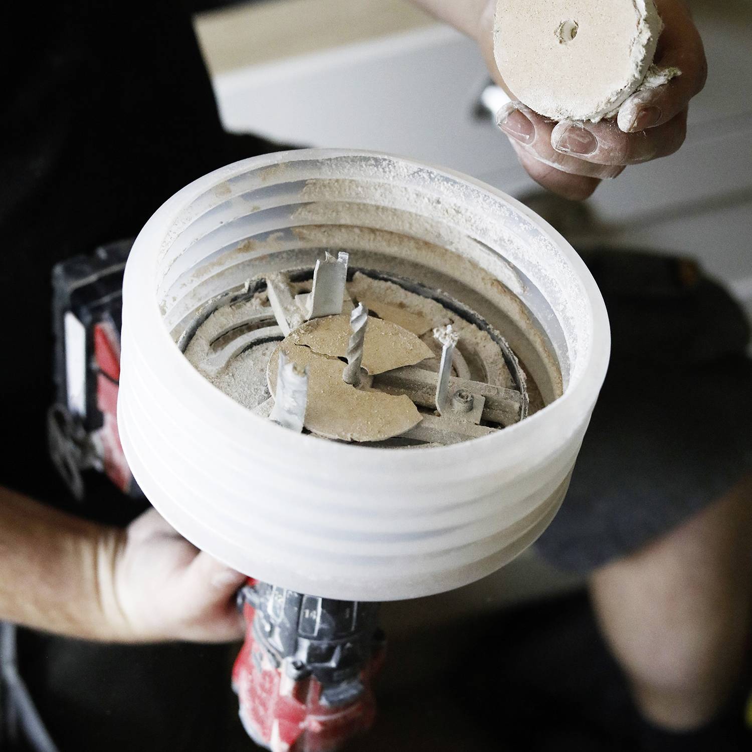 Osoba trzyma dużą piłę otwornicę z usuniętymi elementami tnącymi. Piła jest pokryta pyłem, co sugeruje, że praca została właśnie zakończona.