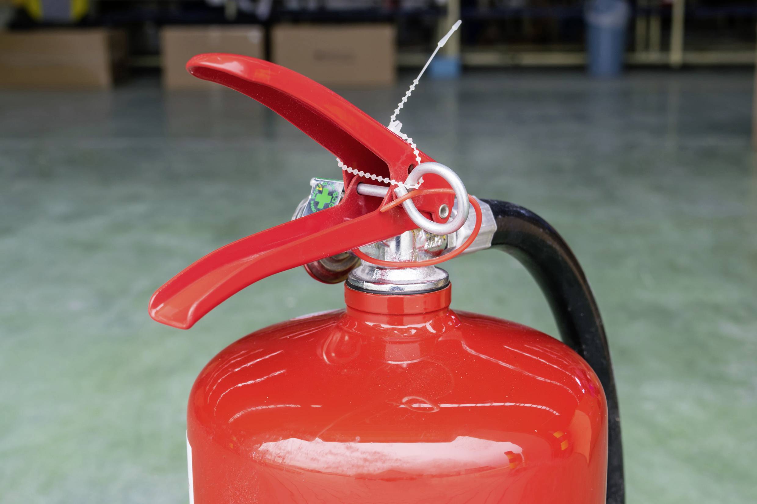 Czerwony gaśnica z zabezpieczonym dźwignią stoi na zielonkawej podłodze.