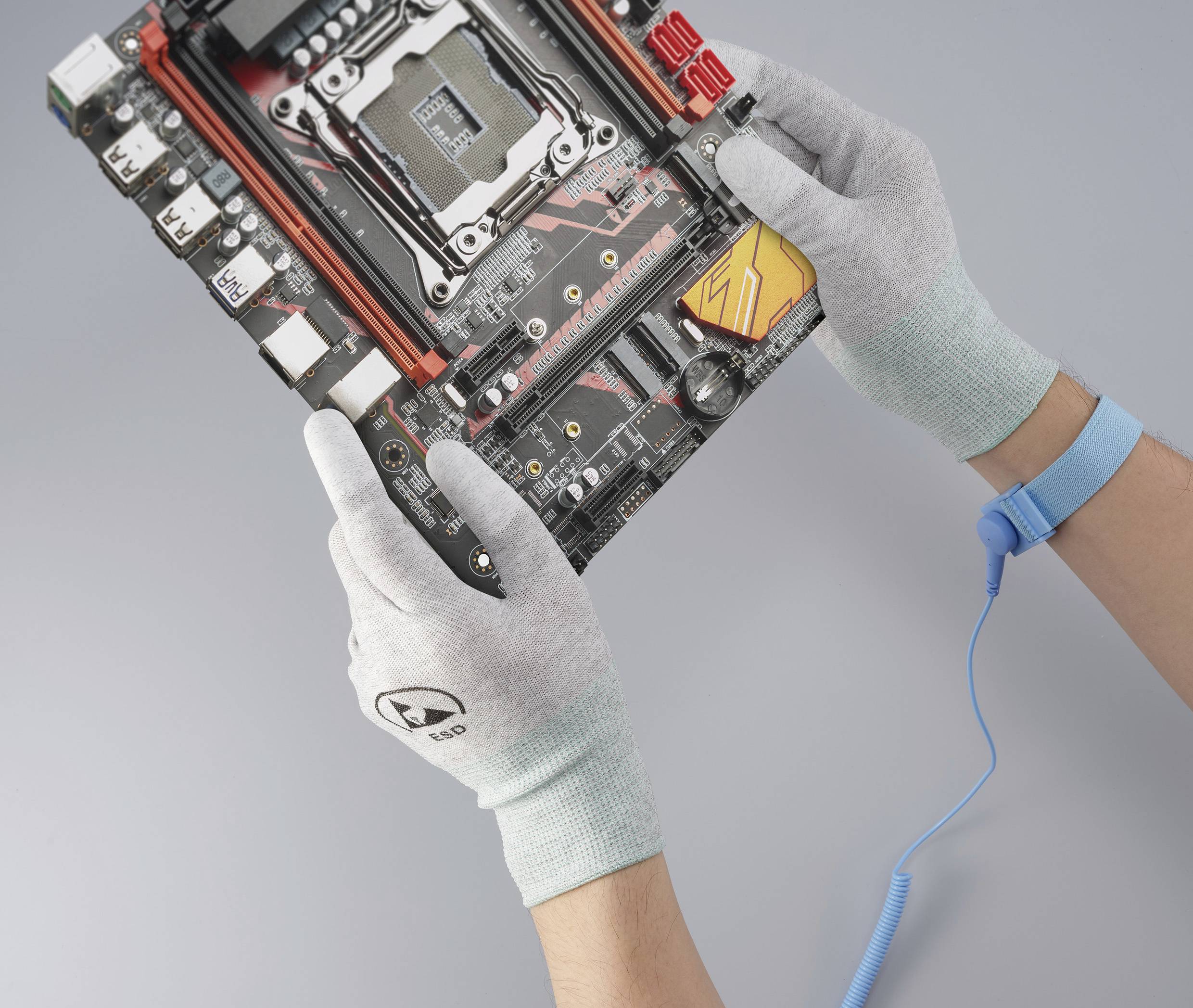 Dwie zabezpieczone rękawiczkami dłonie trzymają płytę główną komputera z widocznym gniazdem procesora i obwodami elektronicznymi. Przewód uziemiający jest przymocowany do nadgarstka.