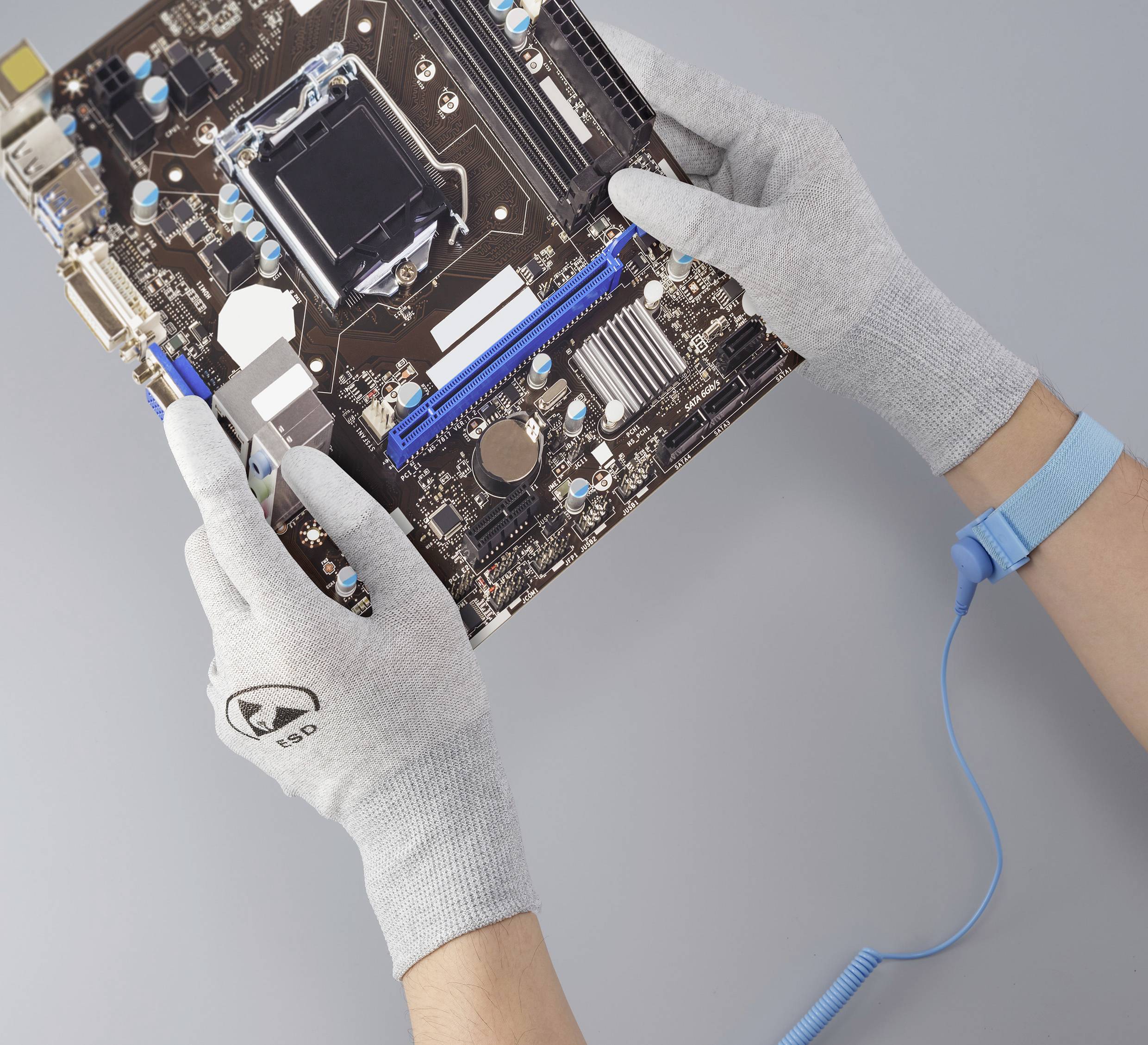 Dwie dłonie w szarych rękawiczkach trzymają płytę główną komputera nad szarą powierzchnią.