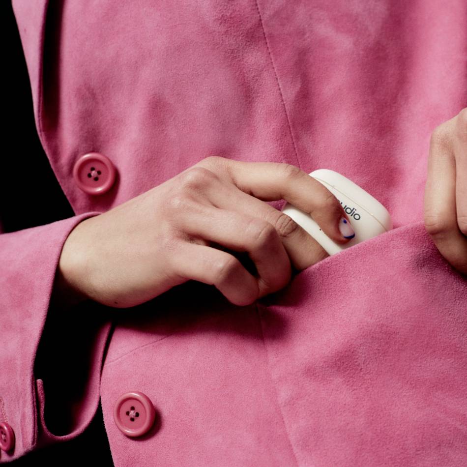 Osoba wkłada białe urządzenie do wewnętrznej kieszeni różowego płaszcza. Urządzenie ma nadruk 'studio'.