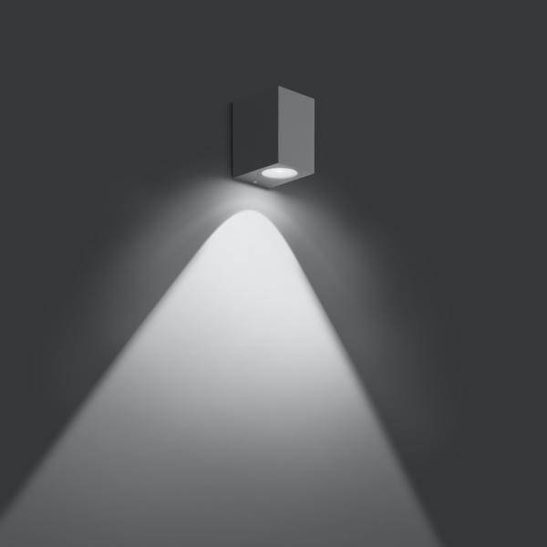 Nowoczesna lampa ścienna rzuca światło w dół na szarą ścianę, tworząc stożkowaty blask.