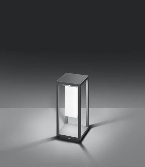 Nowoczesna lampa stojąca o geometrycznym designie, jasno świecąca w ciemnym pomieszczeniu. Struktura wykonana jest z metalu i szkła.